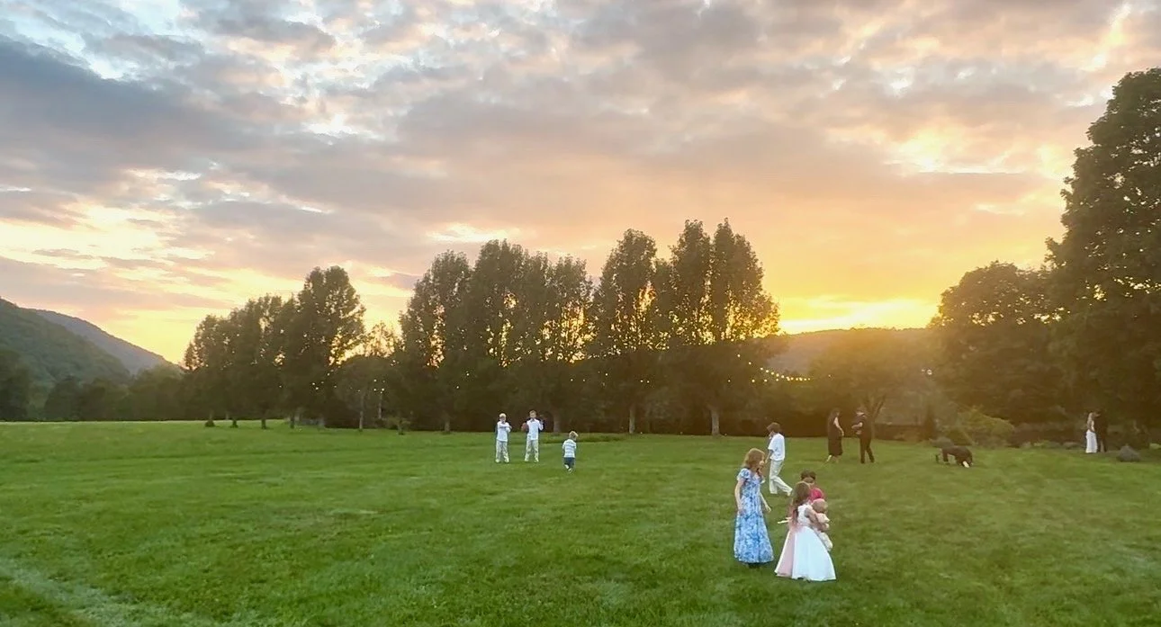 Children running on the lawn as the sun goes down behind the poplars