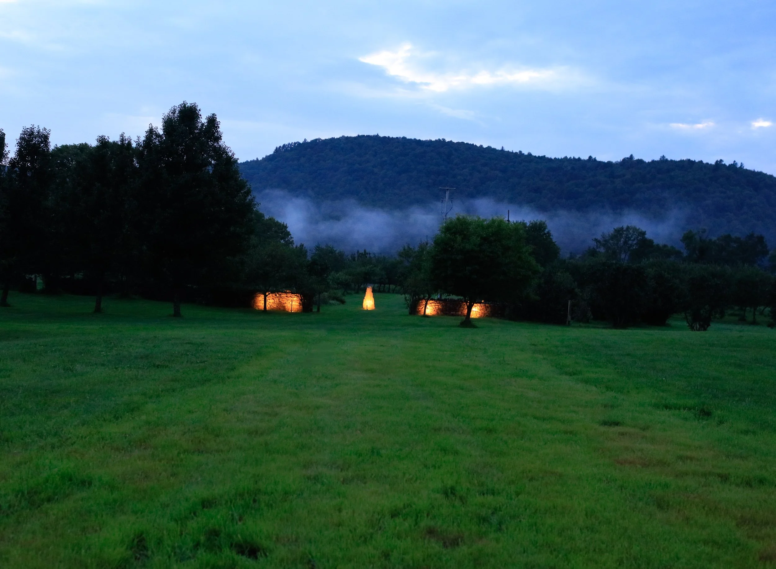 Lanterns lit along the field at dusk, cloud lying along the mountain