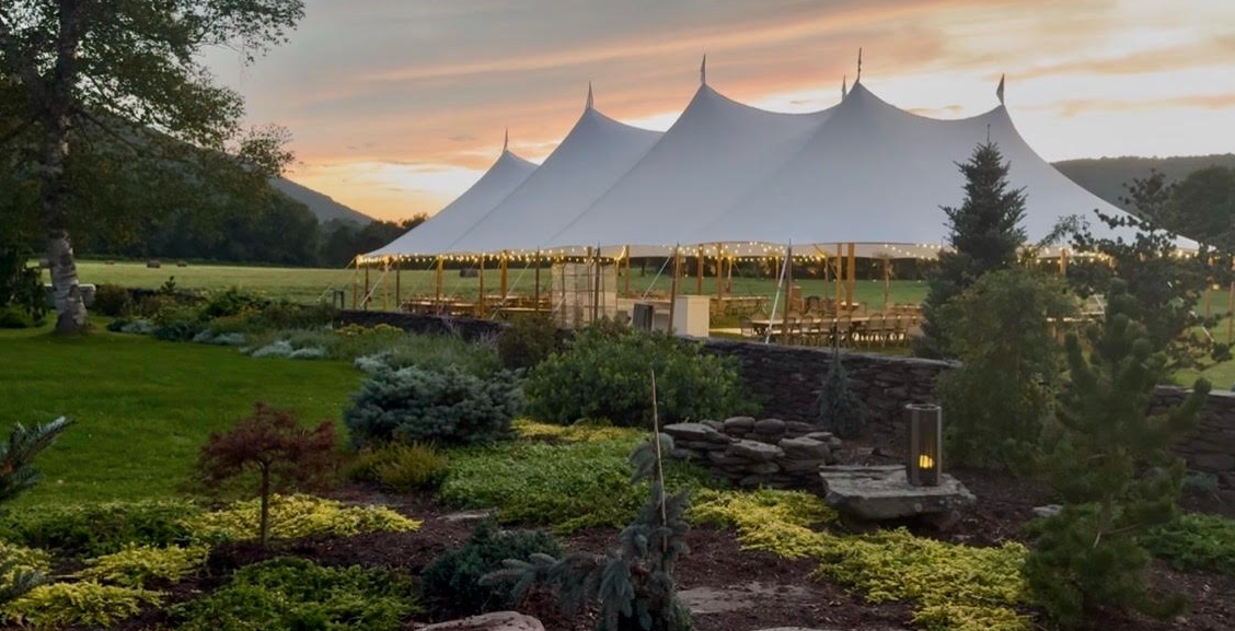 Sailcloth tents lit from within at sunset, the garden in the foreground