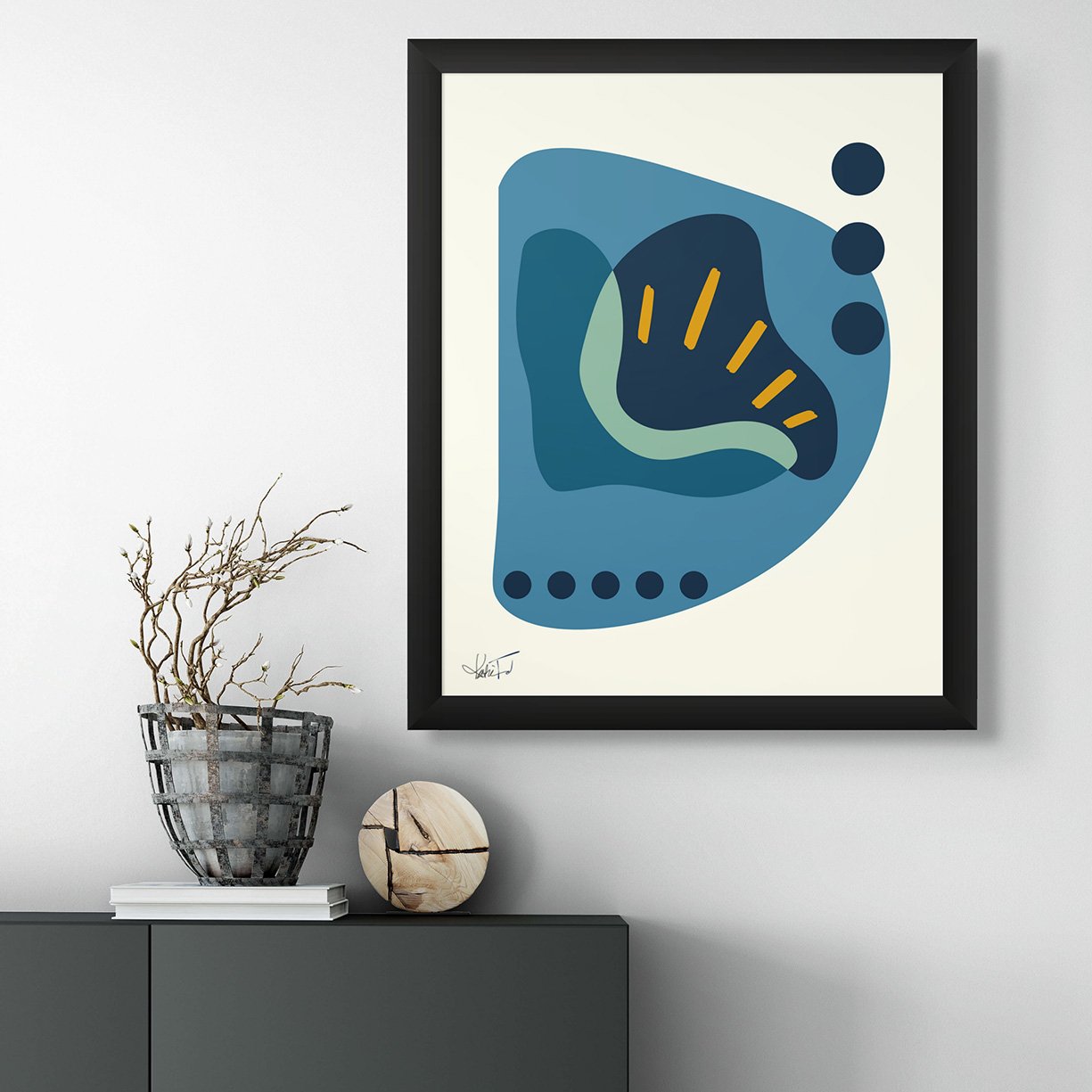 Framed geometric abstract art print in blue, teal, and orange, displayed above a modern console table with decorative elements in a minimalist setting.