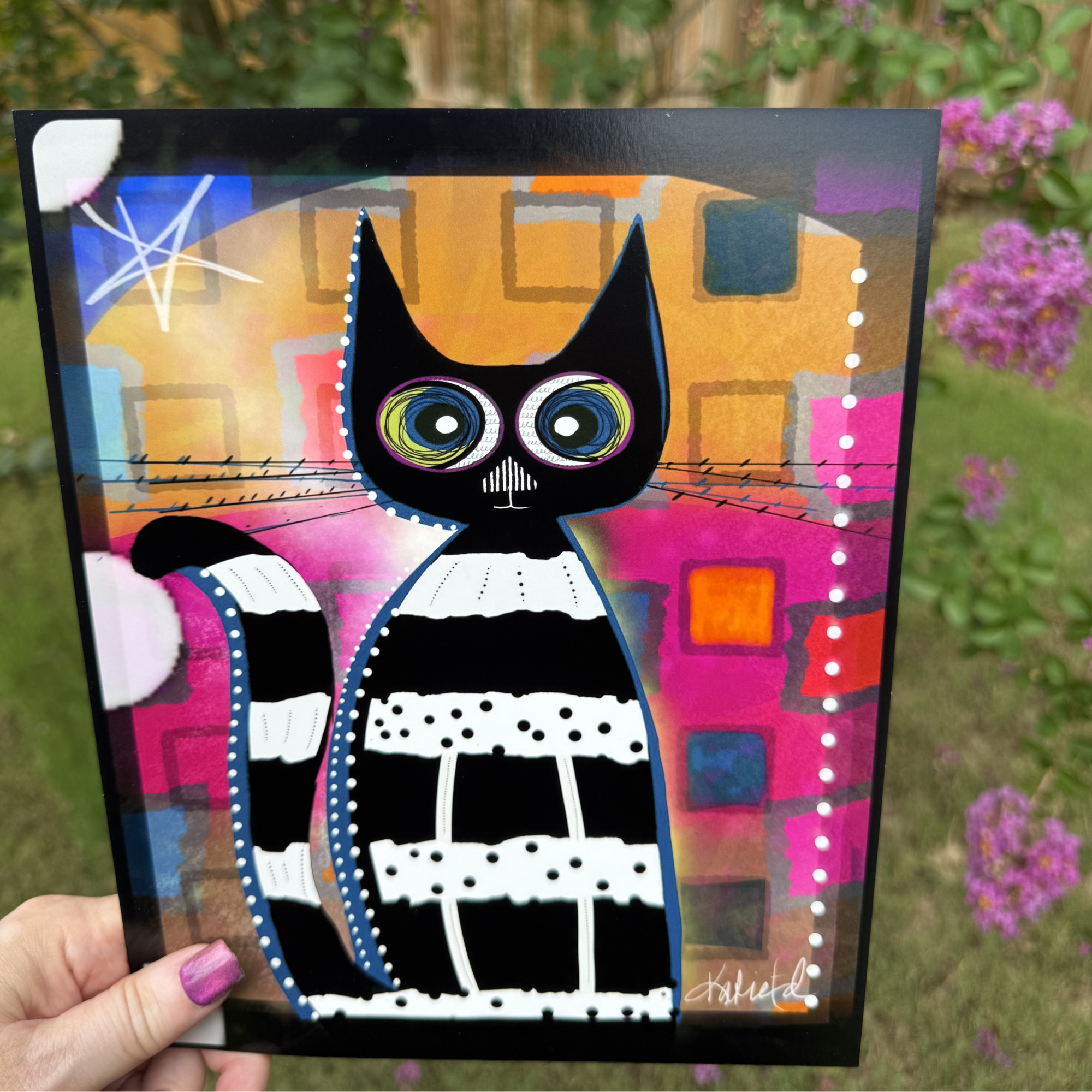 Whimsical black-and-white striped cat art print by Wild Thorn Collective, photographed outdoors with purple flowers.