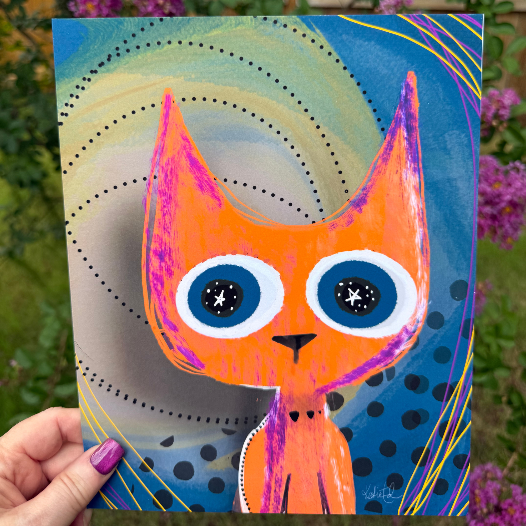 Stars in her Eyes whimsical cat art print by Wild Thorn Collective photographed outdoors among purple flowers.