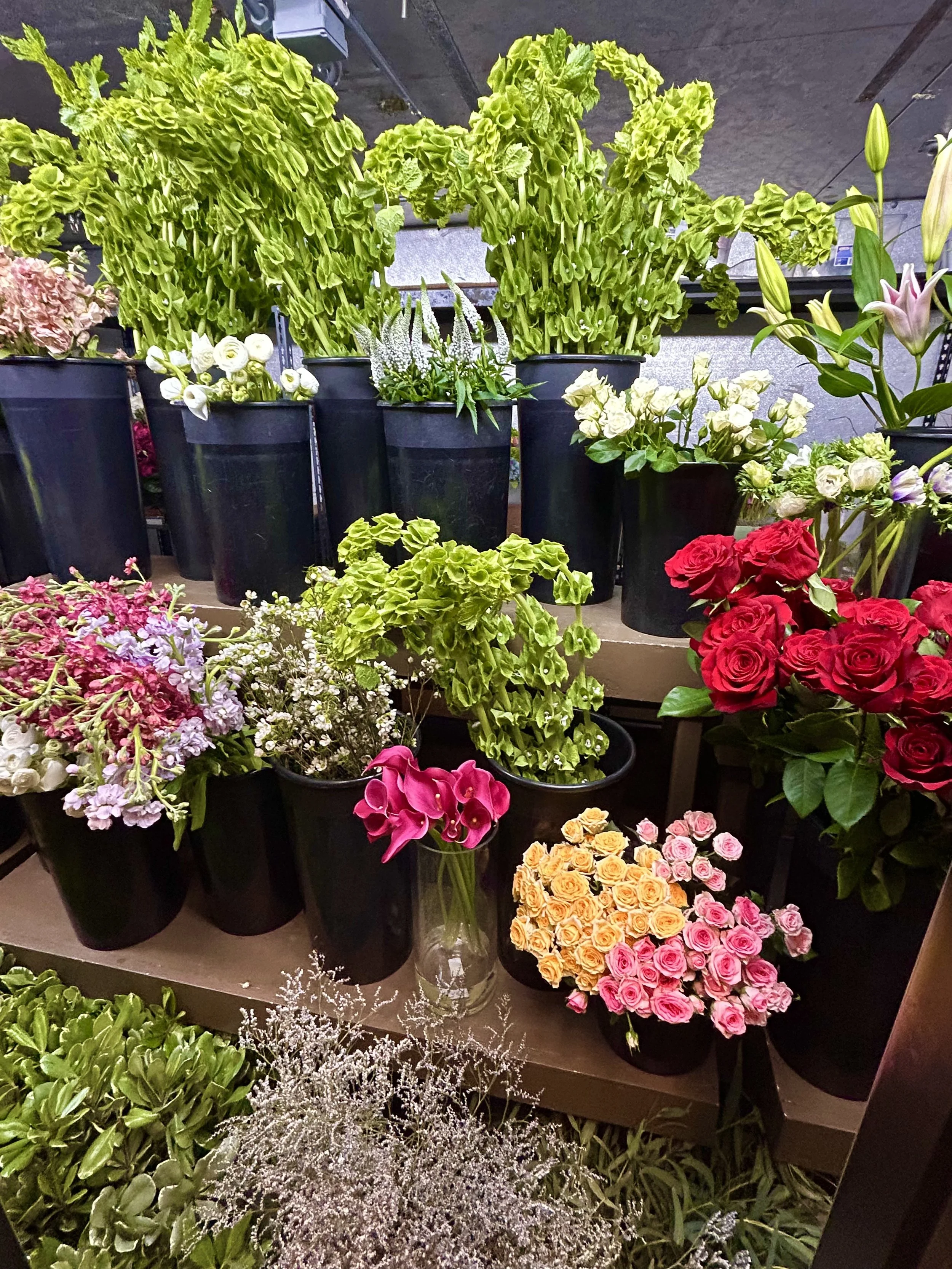 Various potted flowers including roses, calla lilies, and other colorful blooms arranged on shelves in a flower shop.