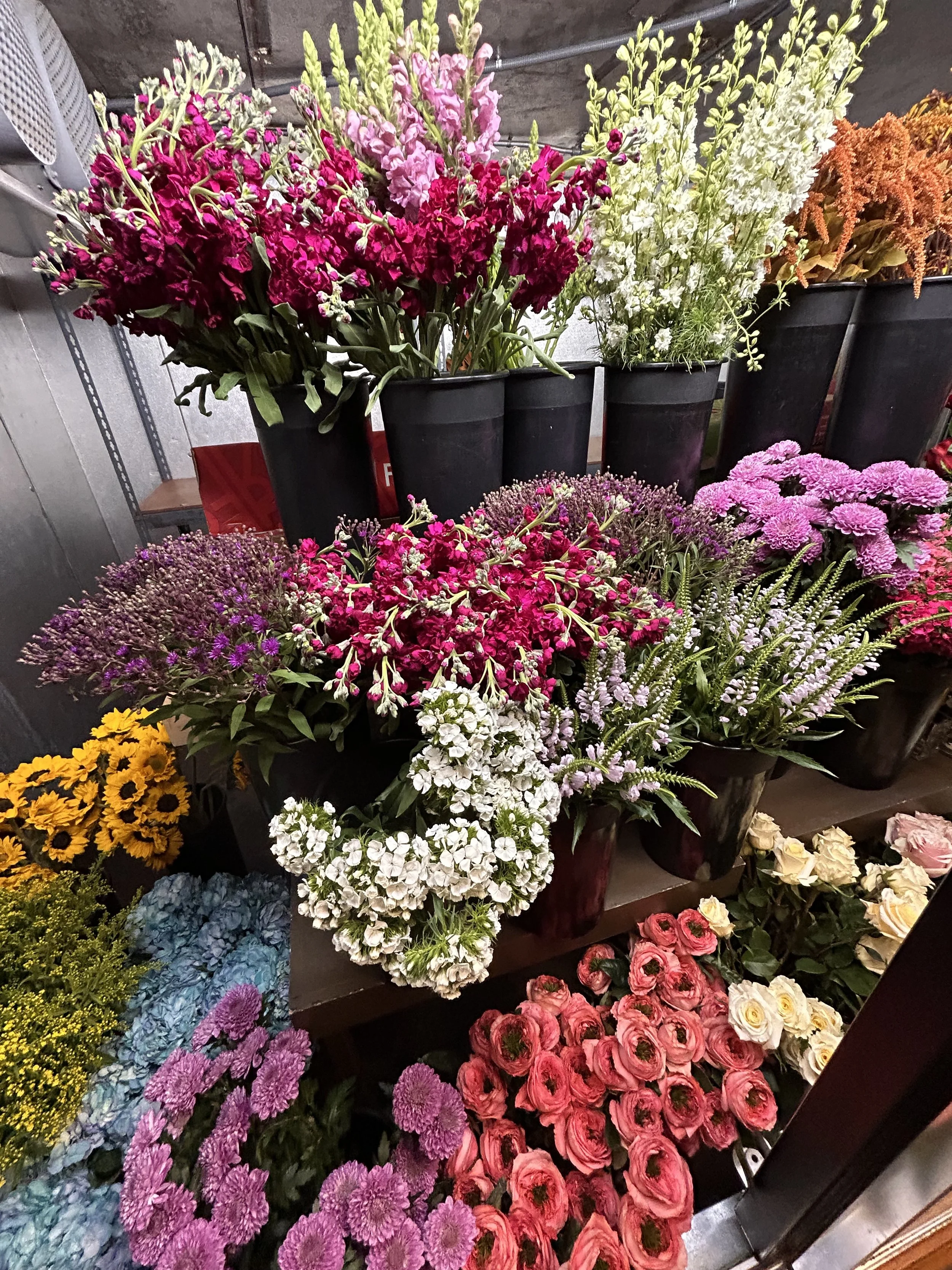 Various colorful flowers arranged in black buckets on a shelf at a florist shop.