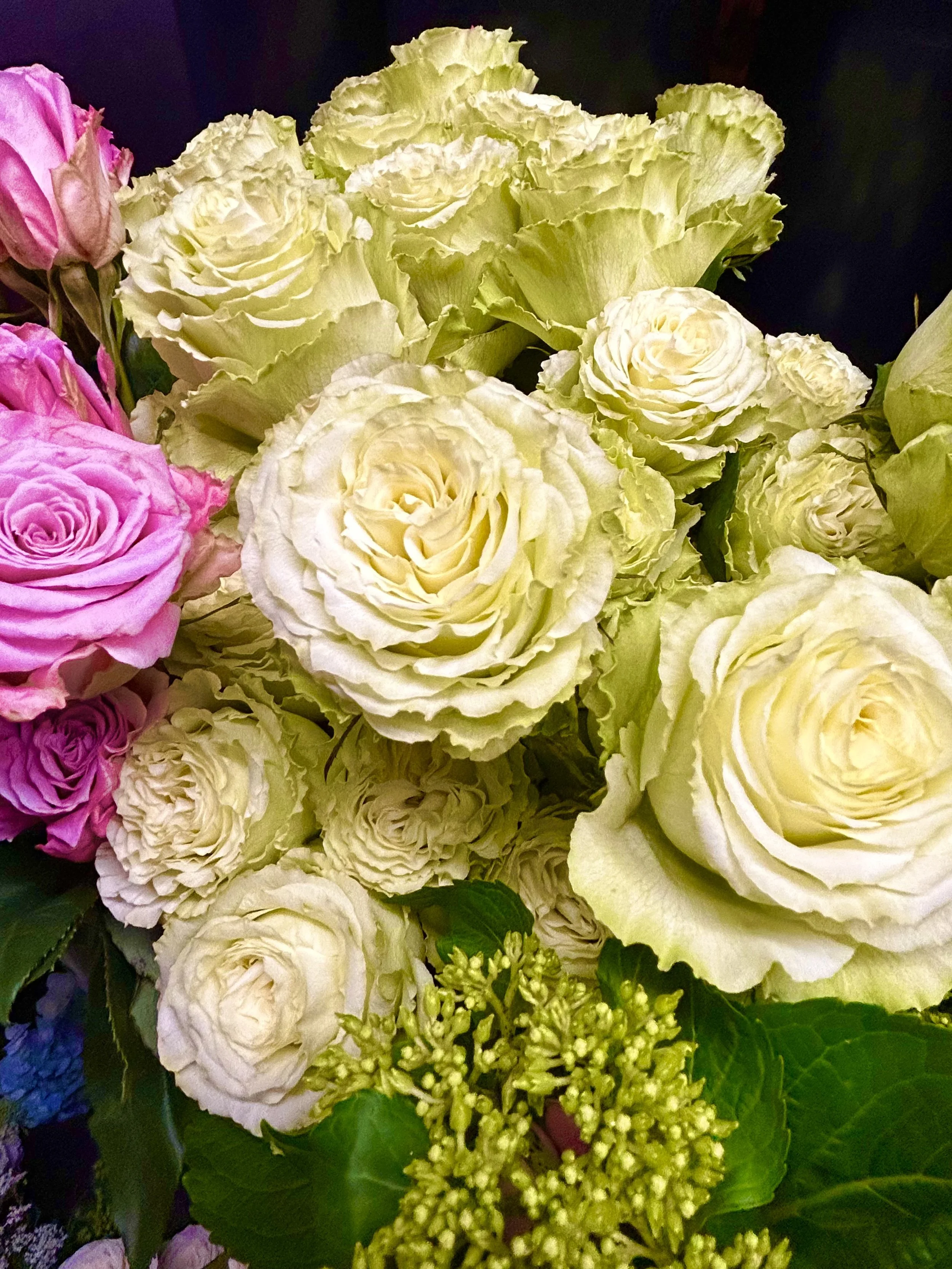 A bouquet of cream-colored roses and green ornamental cabbage, accented with pink roses and green foliage.