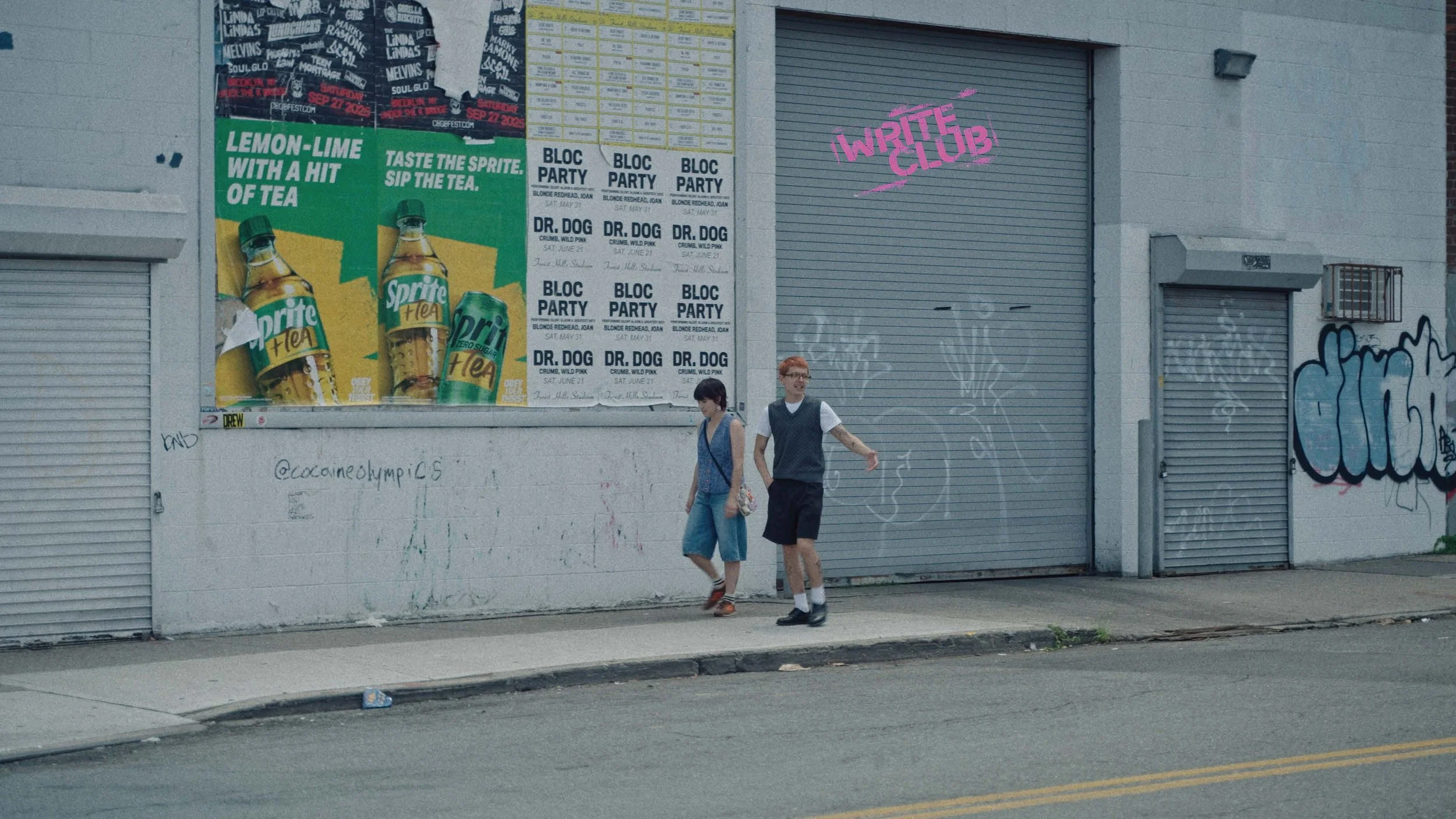 Two young people walking past a building with posters and graffiti. The posters include advertisements for Sprite zero, block parties, and a club called 'Write Club'. The building has a metal door with pink graffiti and a smaller window with an air conditioning unit.