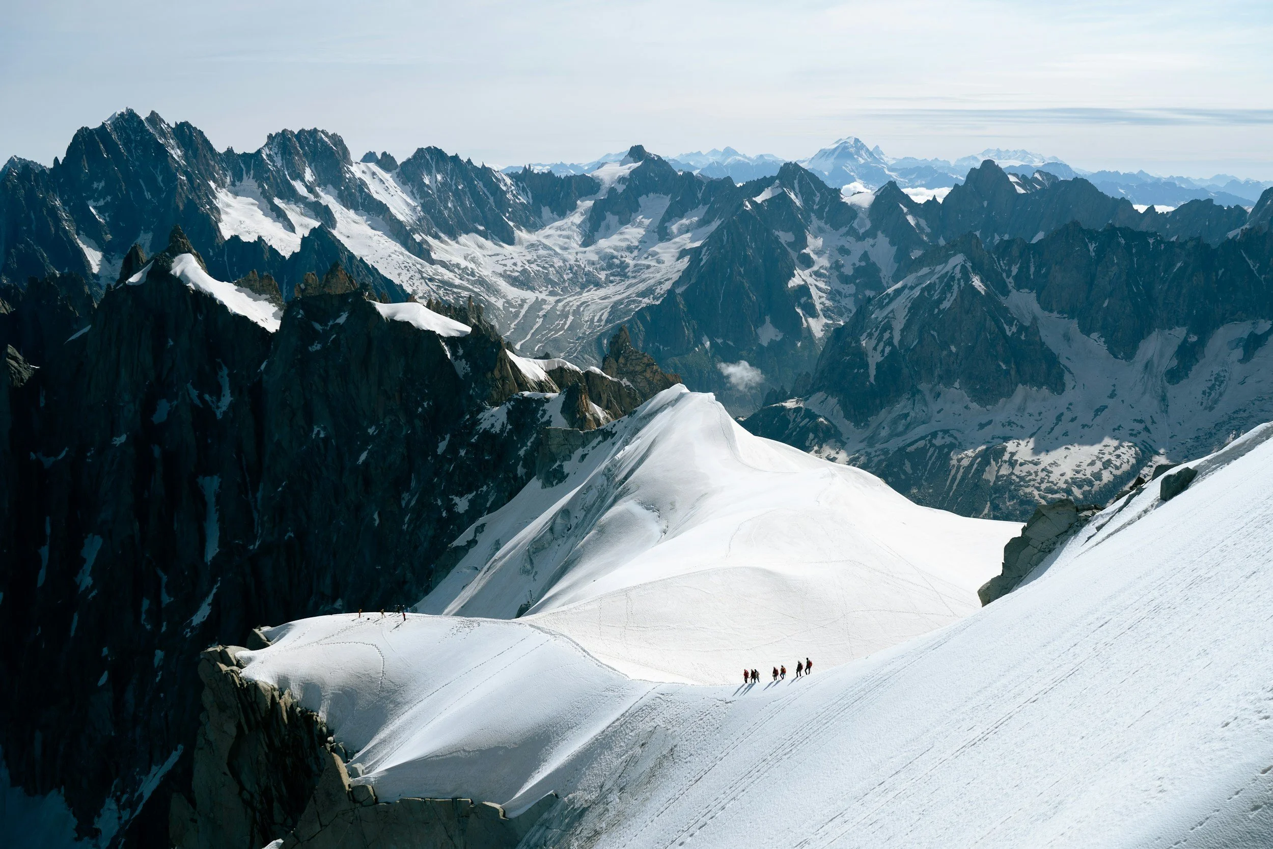 Snow-covered mountain range with a group of climbers trekking on a glacial ridge.