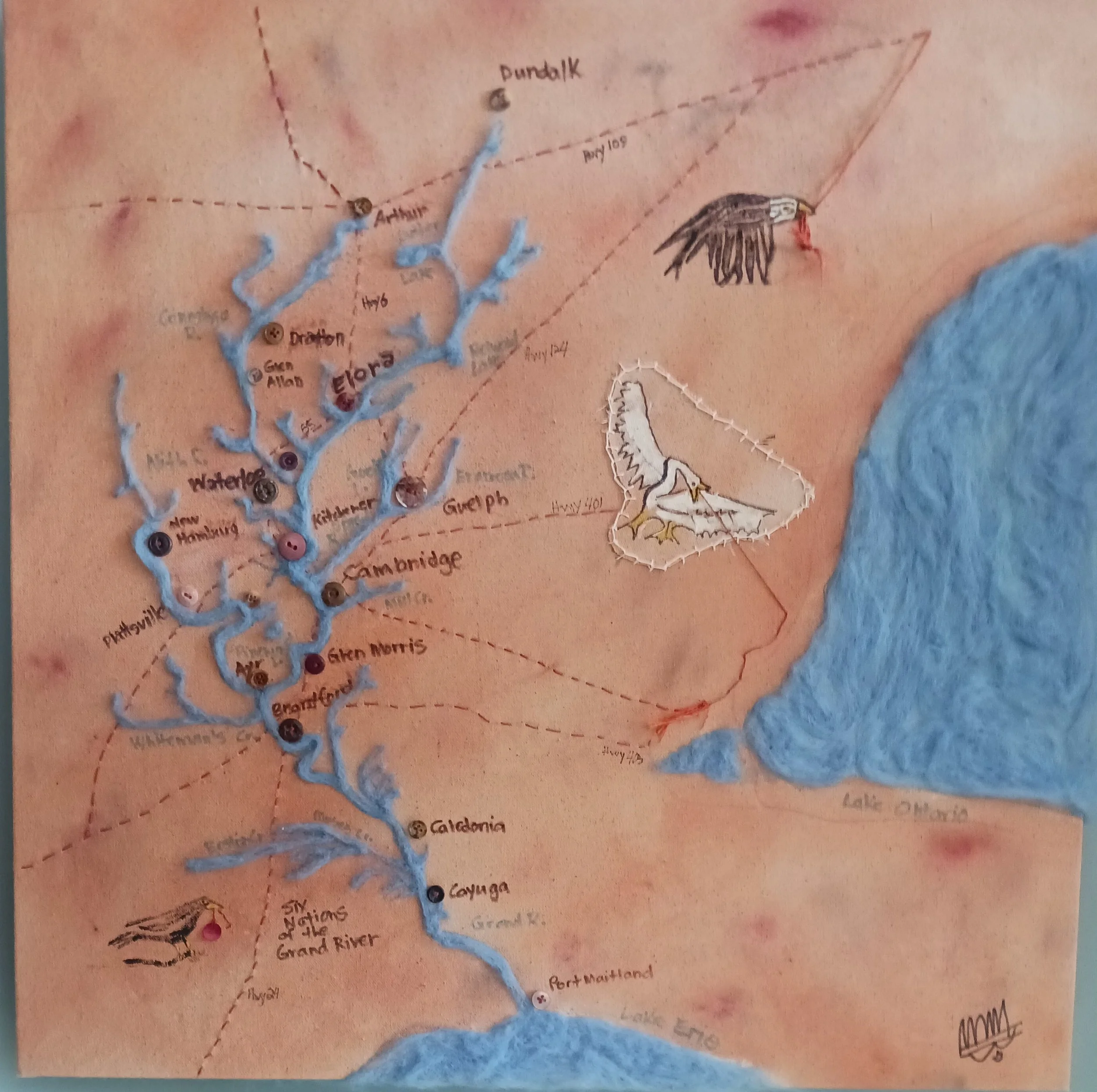 Map of Grand River Watershed on untreated canvas.  Rivers and lakes are felted wool.  Towns and cities are buttons.  Some major highways are embroidered.  The birds are claiming the embroidery thread!
