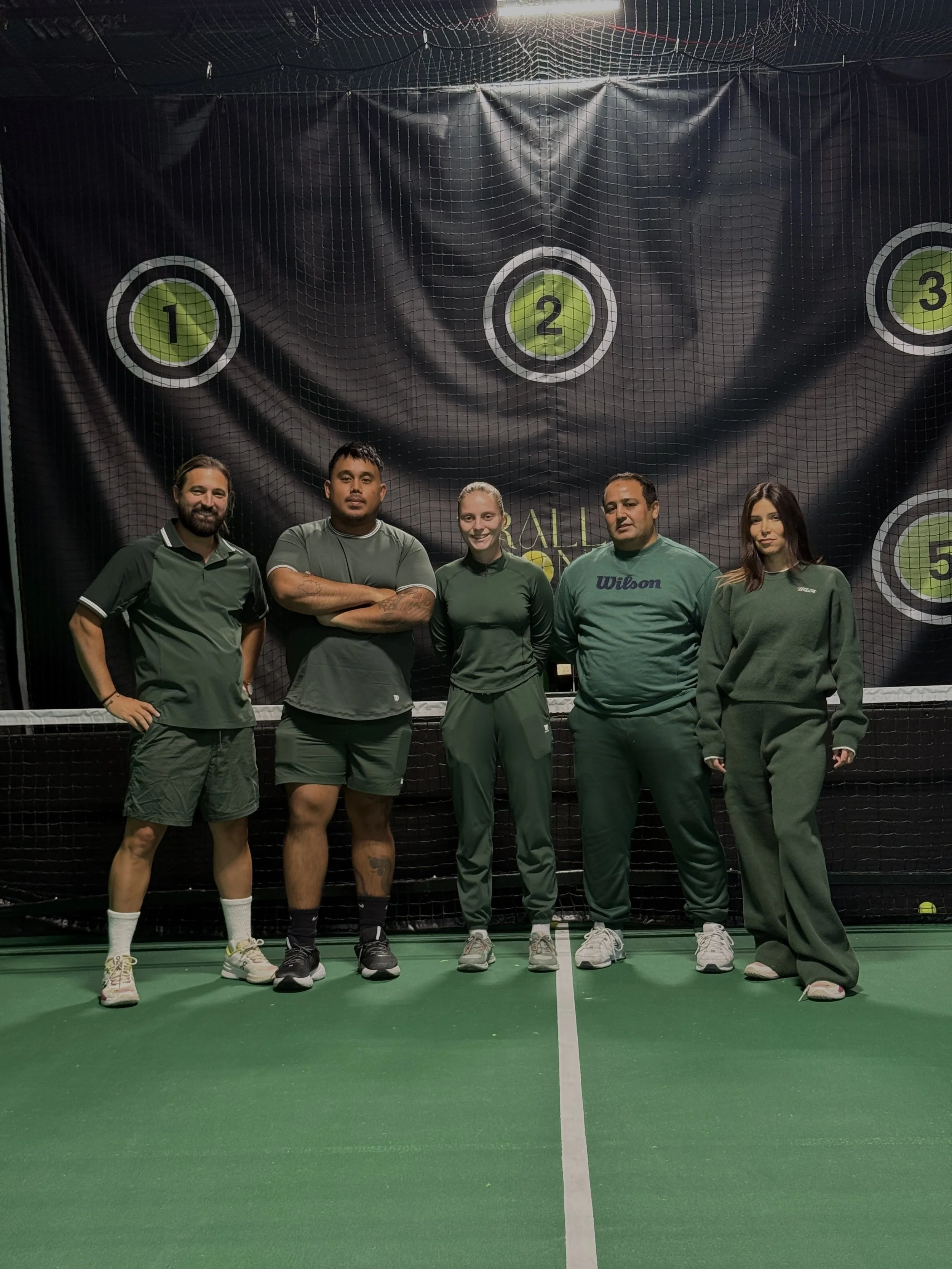 Coach guiding adult player on indoor court beside ball-machine at Rally Zone Jersey City