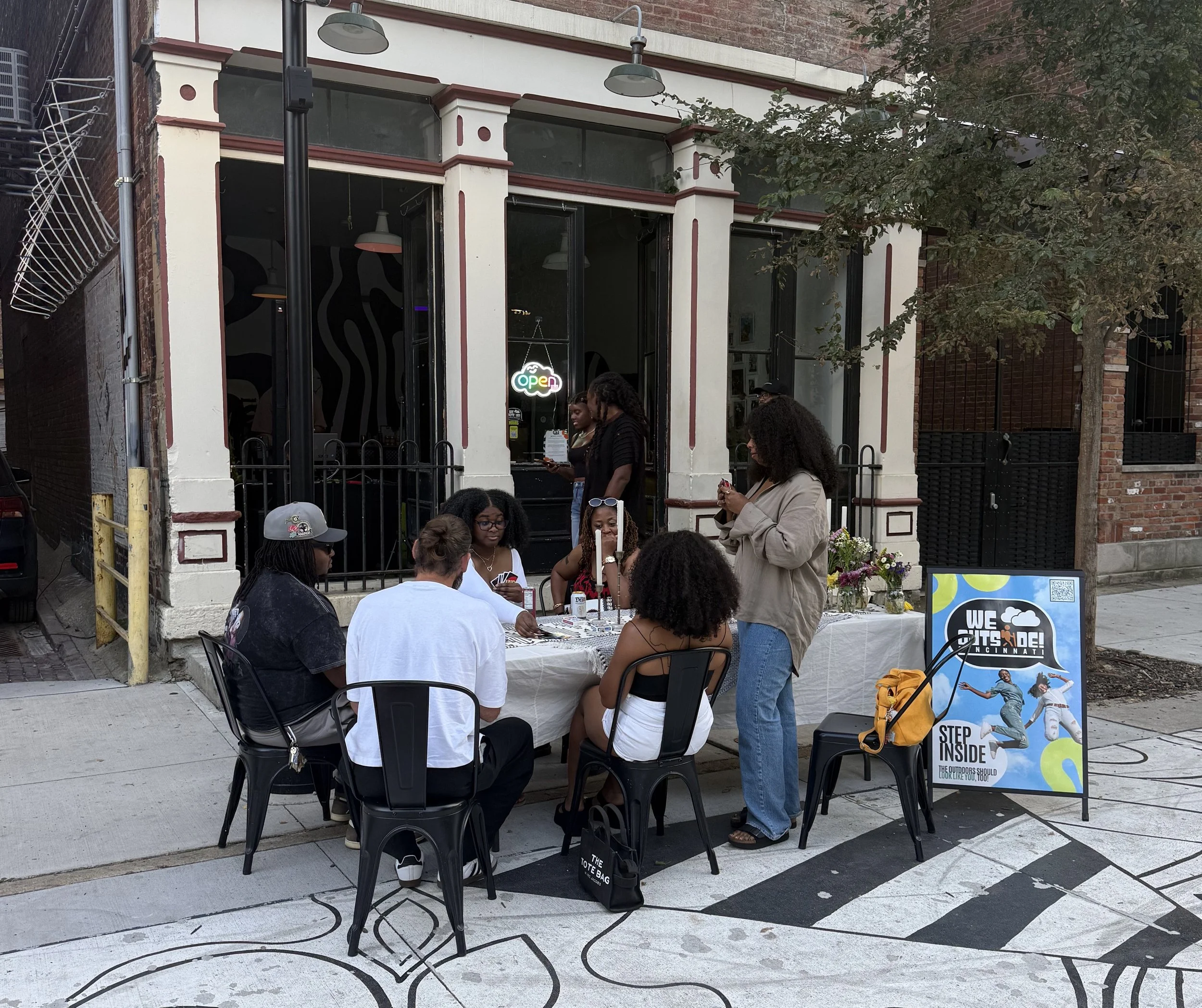 Image taken in front of the We Outside Shop. Taken during a We Outside: After Dark Event. People are playing uno, happy, enjoying being in community.