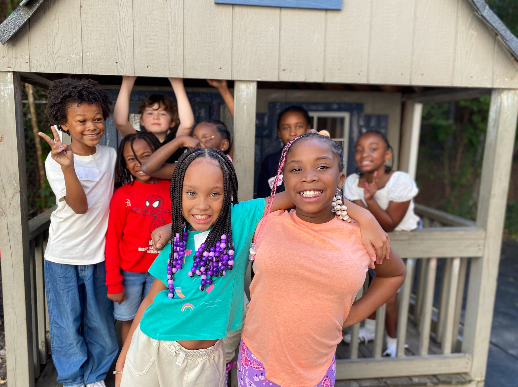 Group of smiling children posing in front of and inside a wooden playhouse.