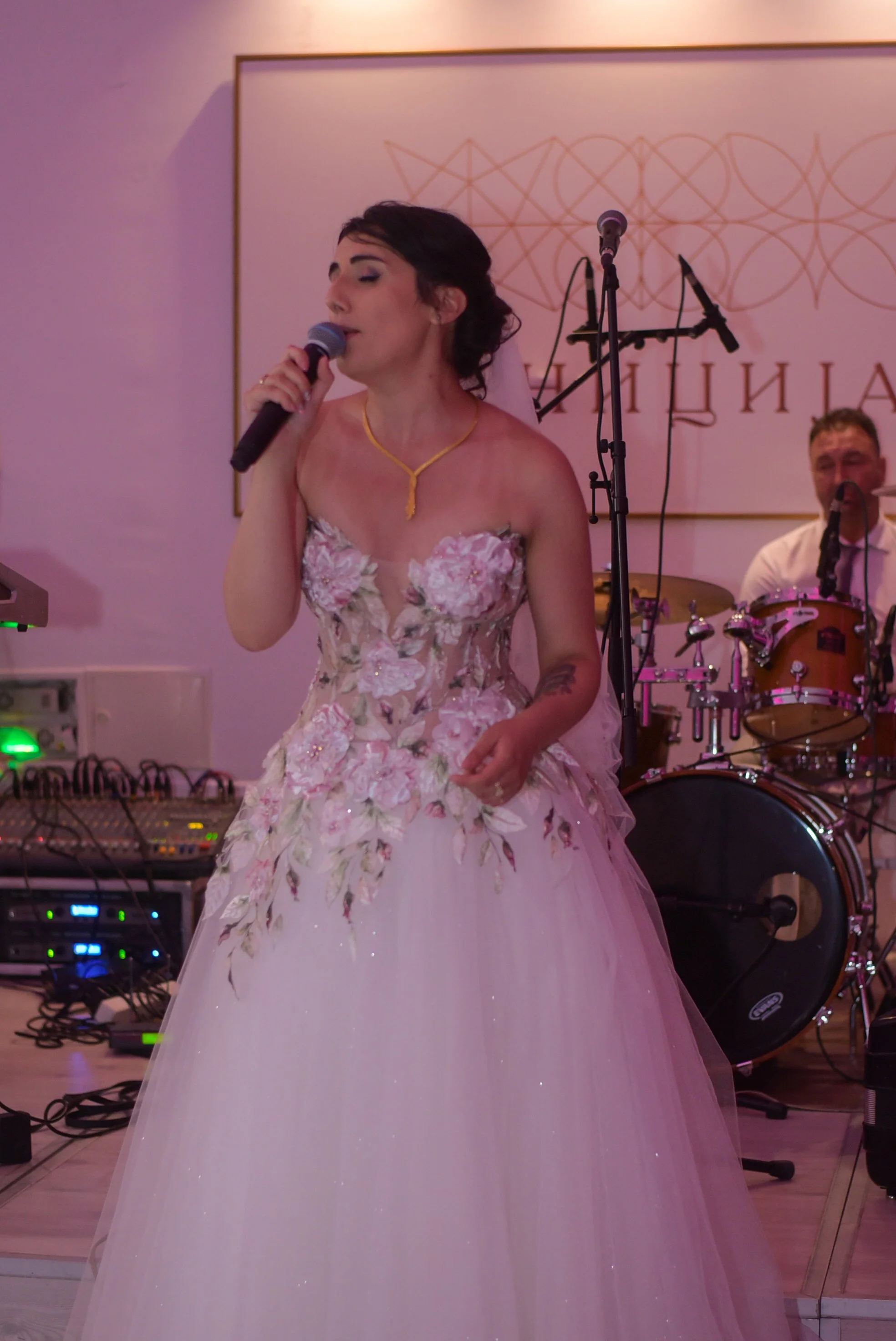 Sängerin in Hochzeitskleid mit Mikrofon vor einer Bühne.