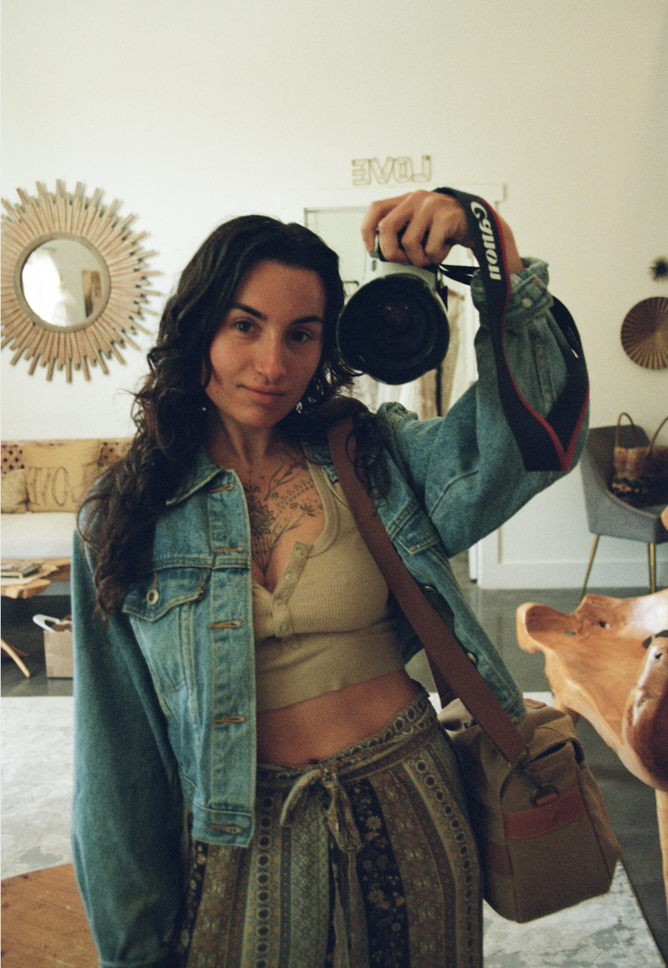 A woman taking a selfie with a camera in a room decorated with wall mirrors and art pieces.