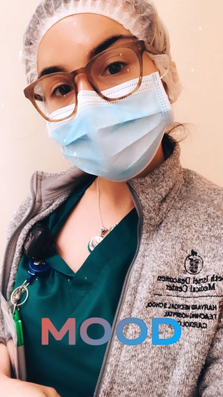 A healthcare worker wearing glasses, a hair cap, a face mask, and scrubs, with the word 'MOOD' written on the image.