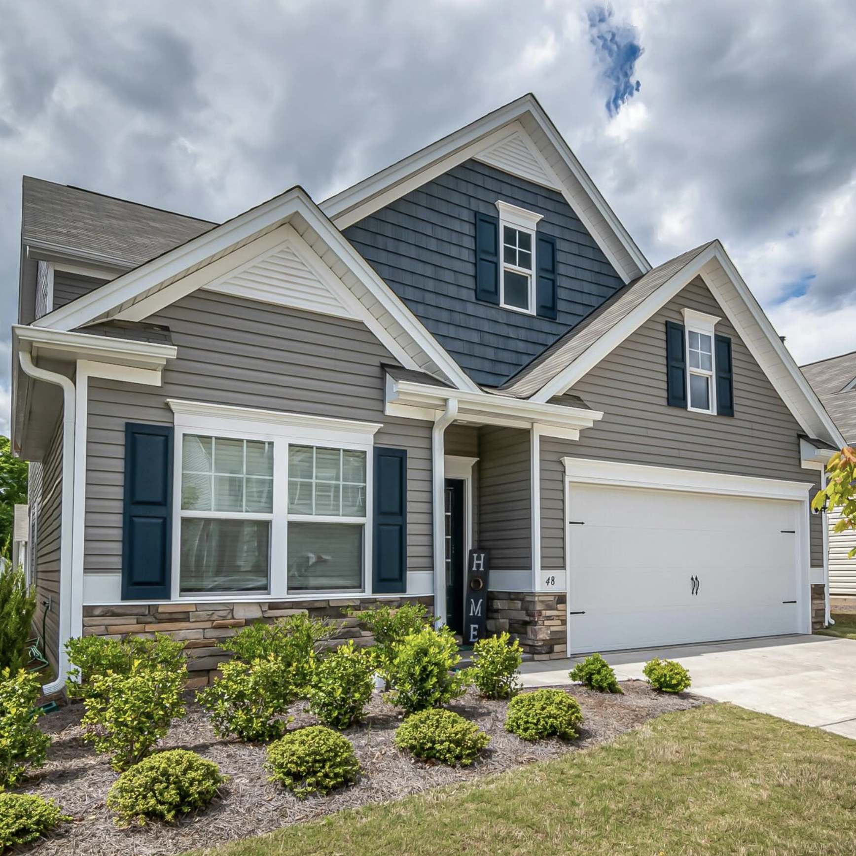 Grey and blue house with blue shutters and a green lawn.