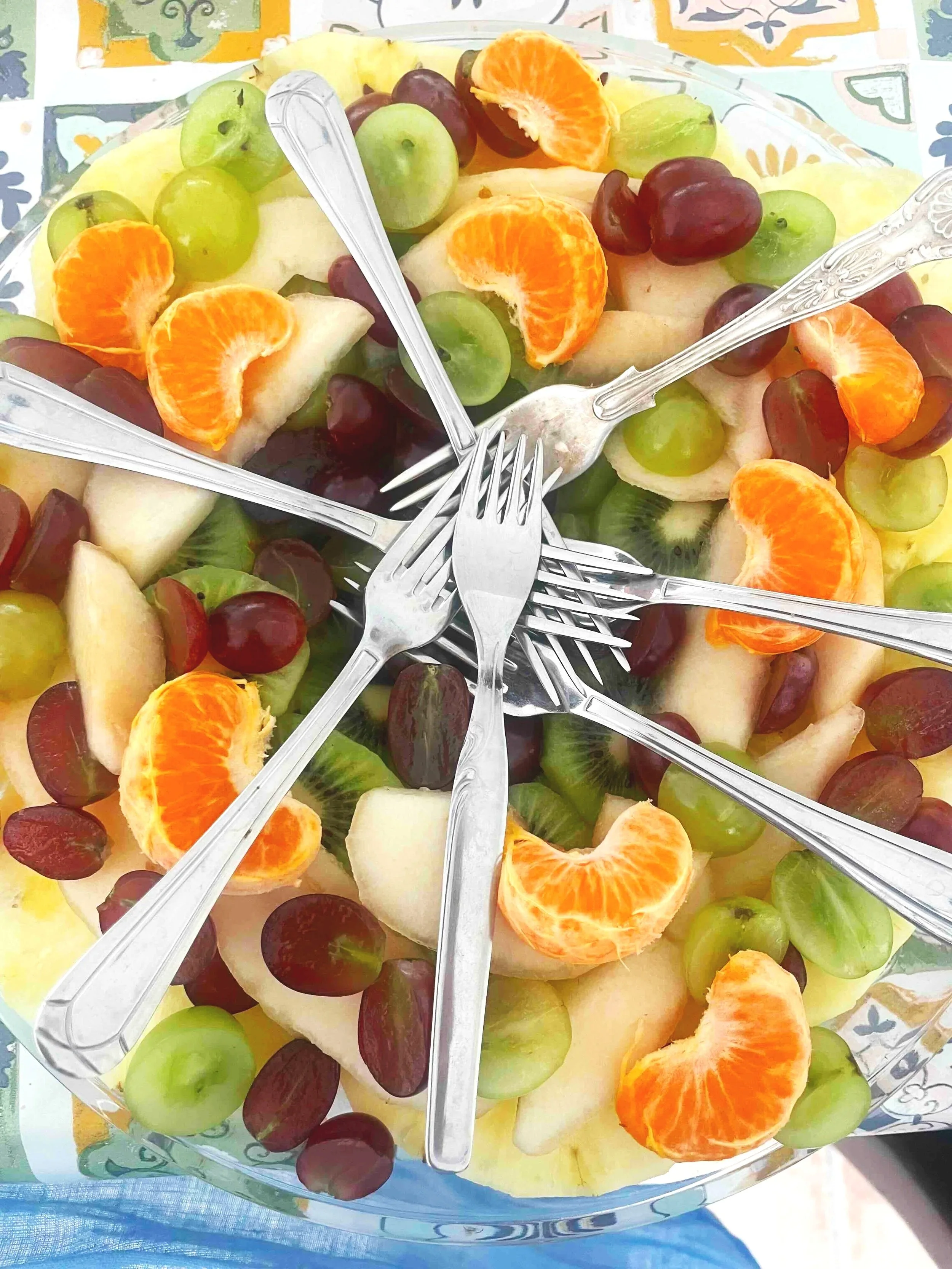 Plate of assorted fruit slices with oranges, grapes, and kiwi, surrounded by several forks.