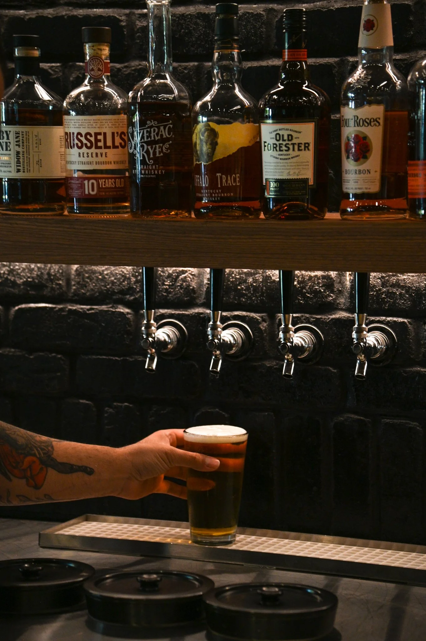 Person pouring a pint of beer from a tap in a bar with whiskey bottles on shelves in the background.