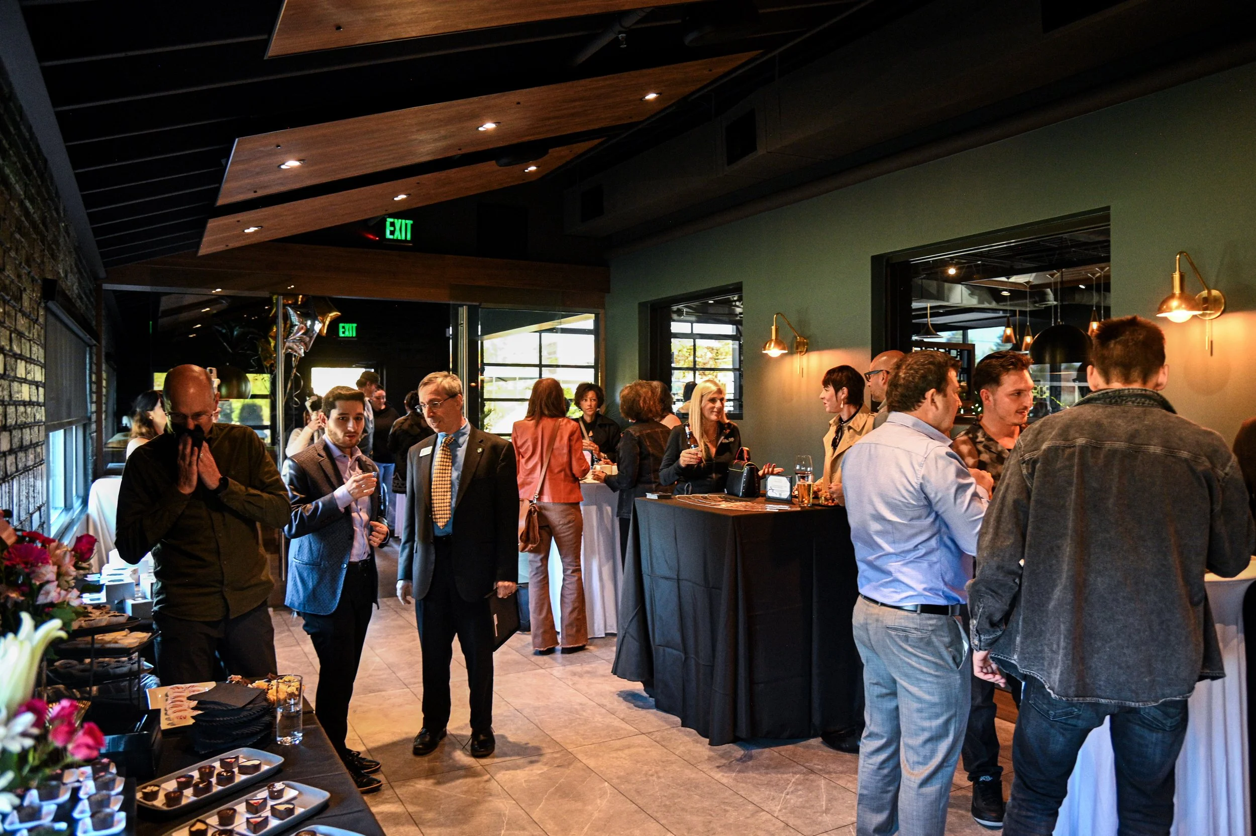 People socializing at a reception with tables of food and drinks in a modern indoor venue.