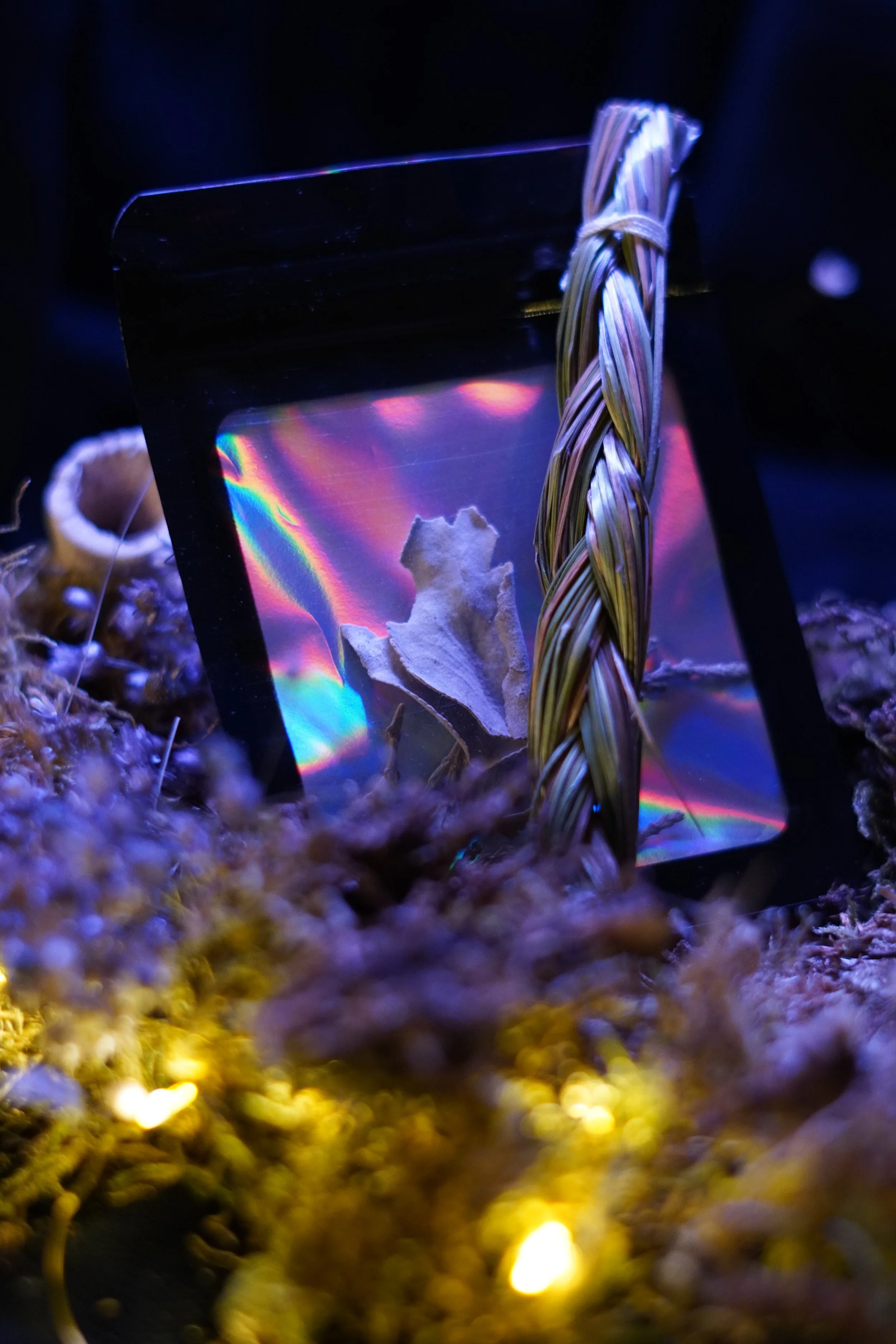 Sweetgrass leaning on a multicolored packet of sage and cedar, on top of a bed of dried flowers and moss