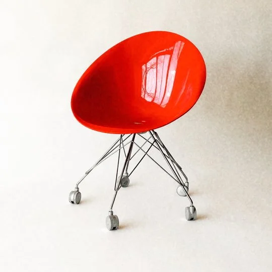 A red modern chair with a curved seat and metal legs with caster wheels, against a plain light background.