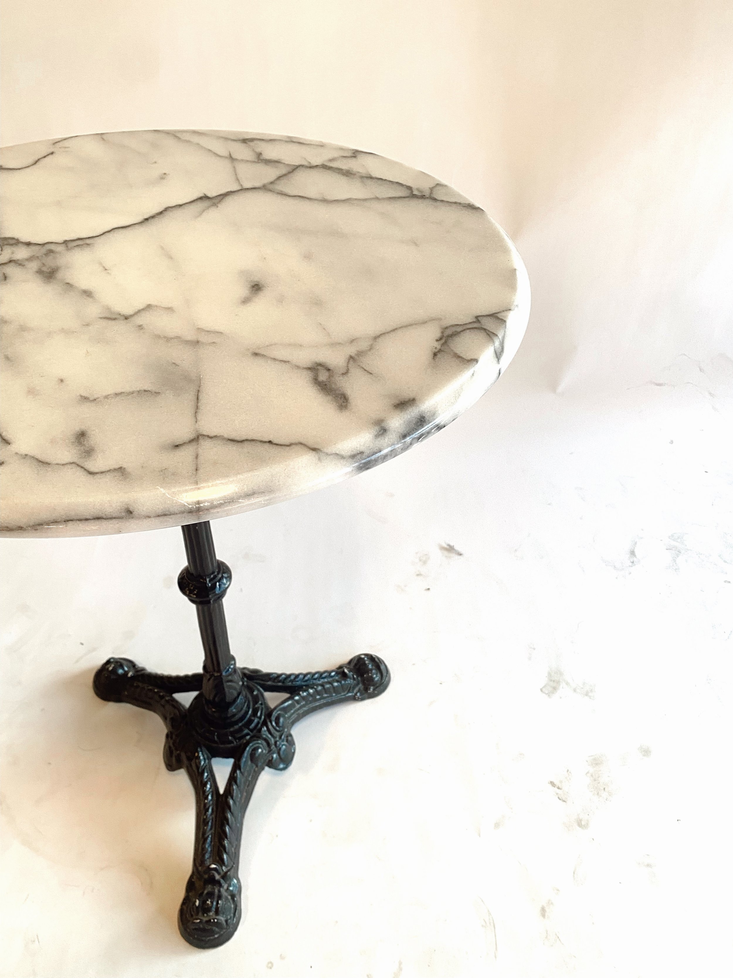 A small round table with a marble top and black decorative iron base, positioned on a white floor.