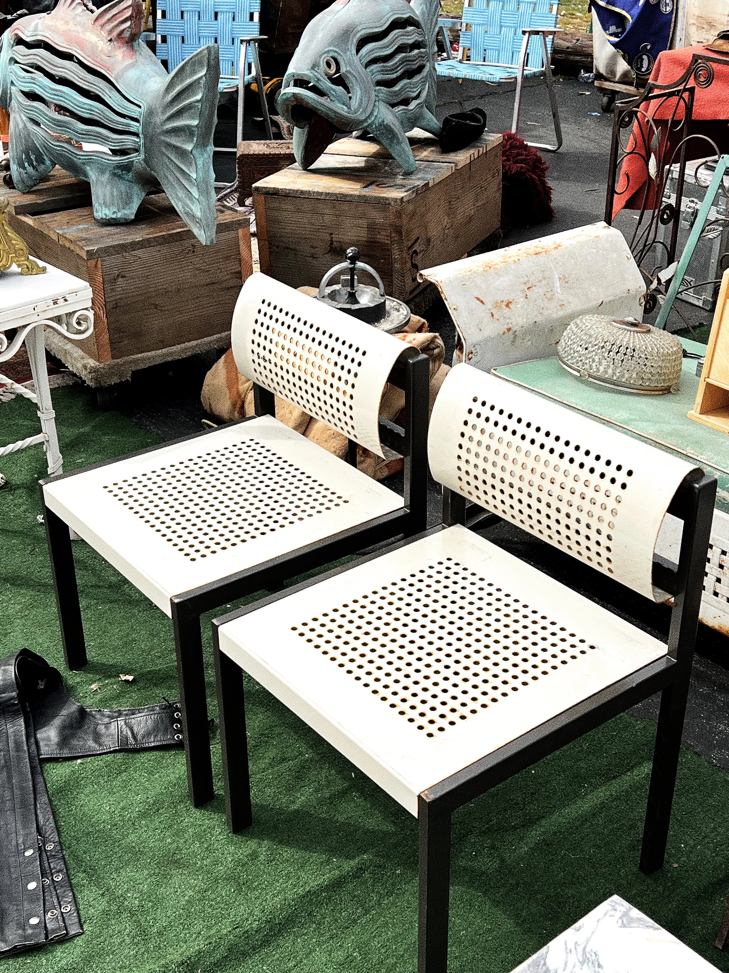 Pair of white chairs with black frames and perforated seats and backrests at a flea market.