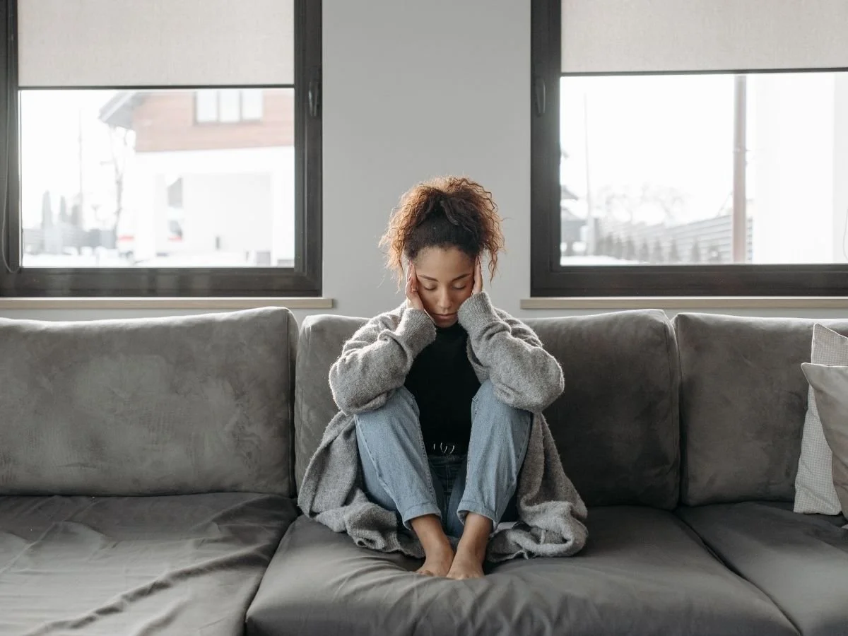 A woman sits on the couch holding her head with fatigue