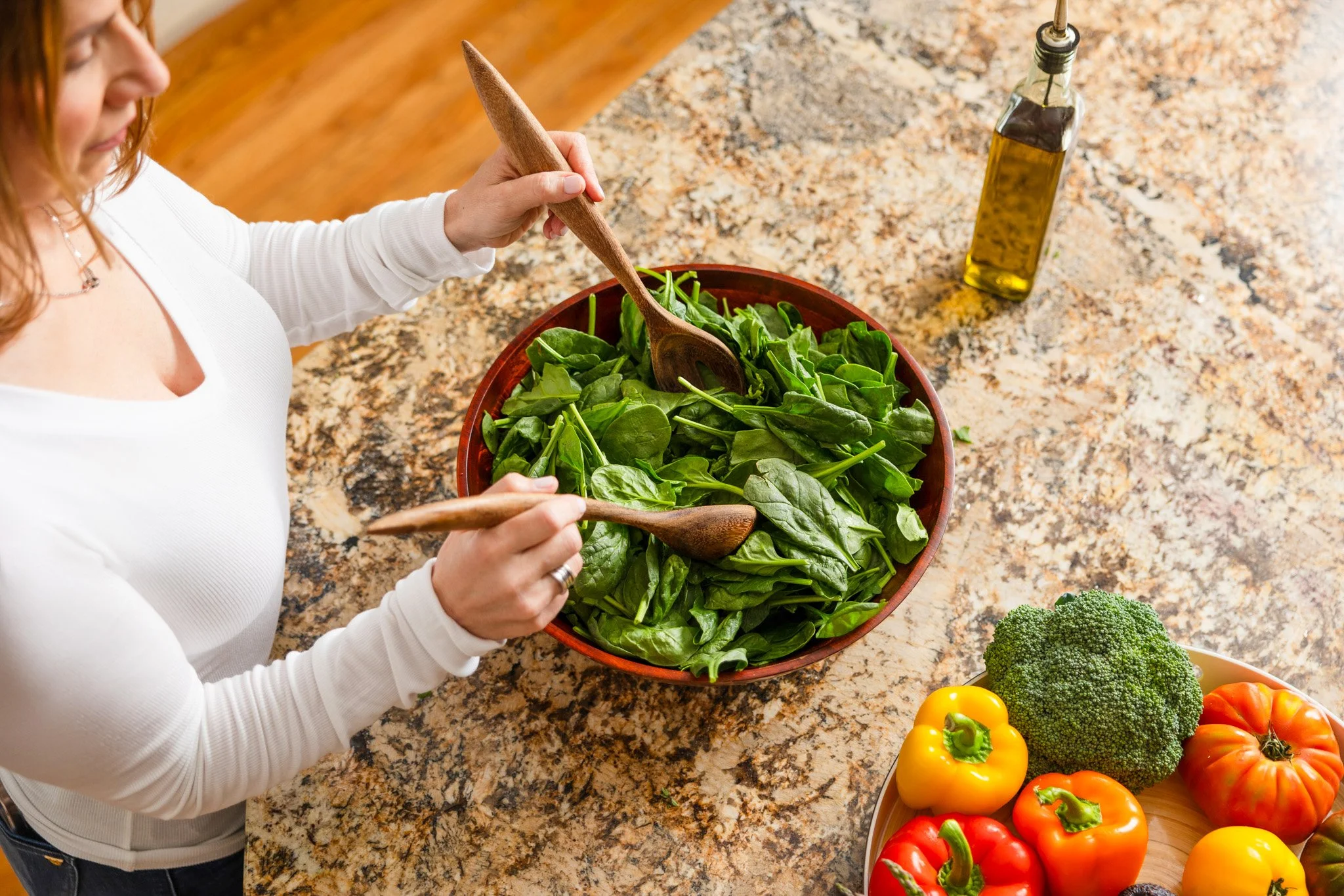 An overhead shot of a woman tossing leafy greens in a bowl to help post-surgical healing.
