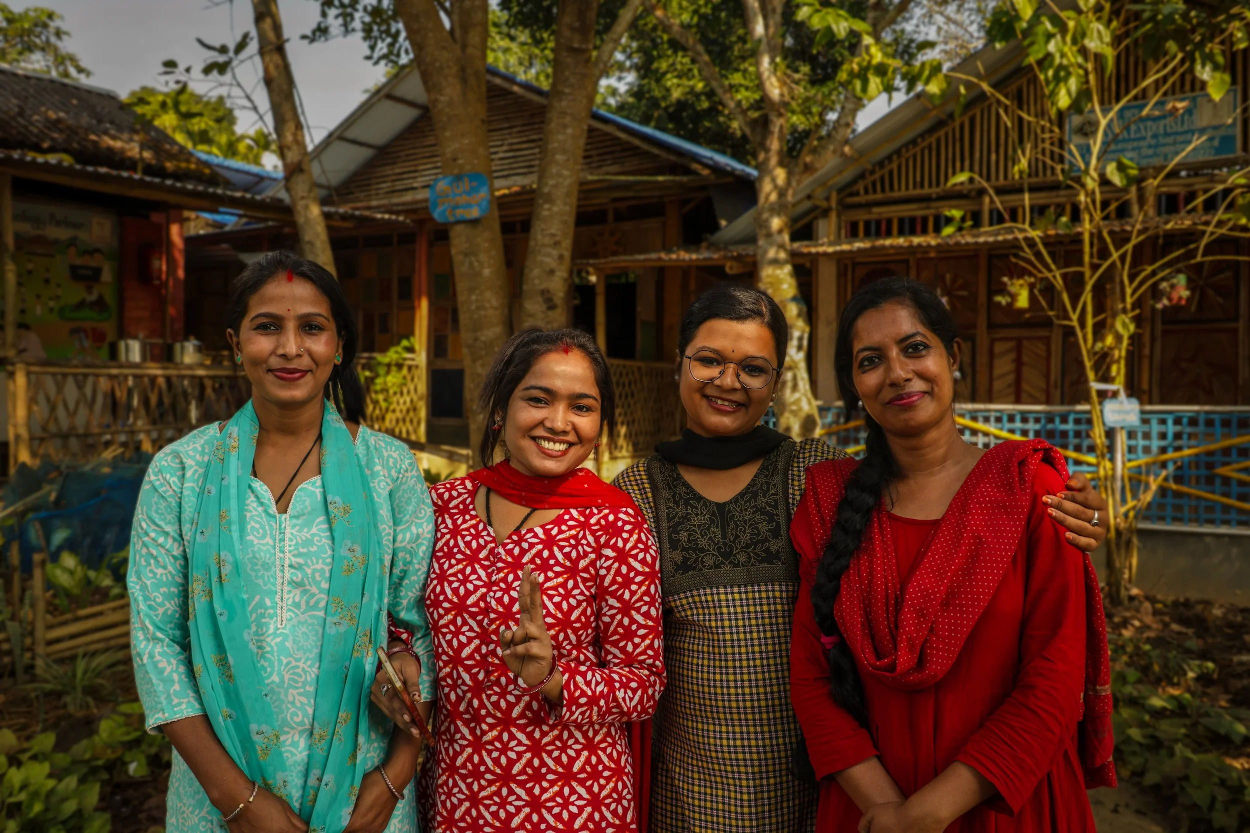 four female teachers standing in front of a bamboo school building