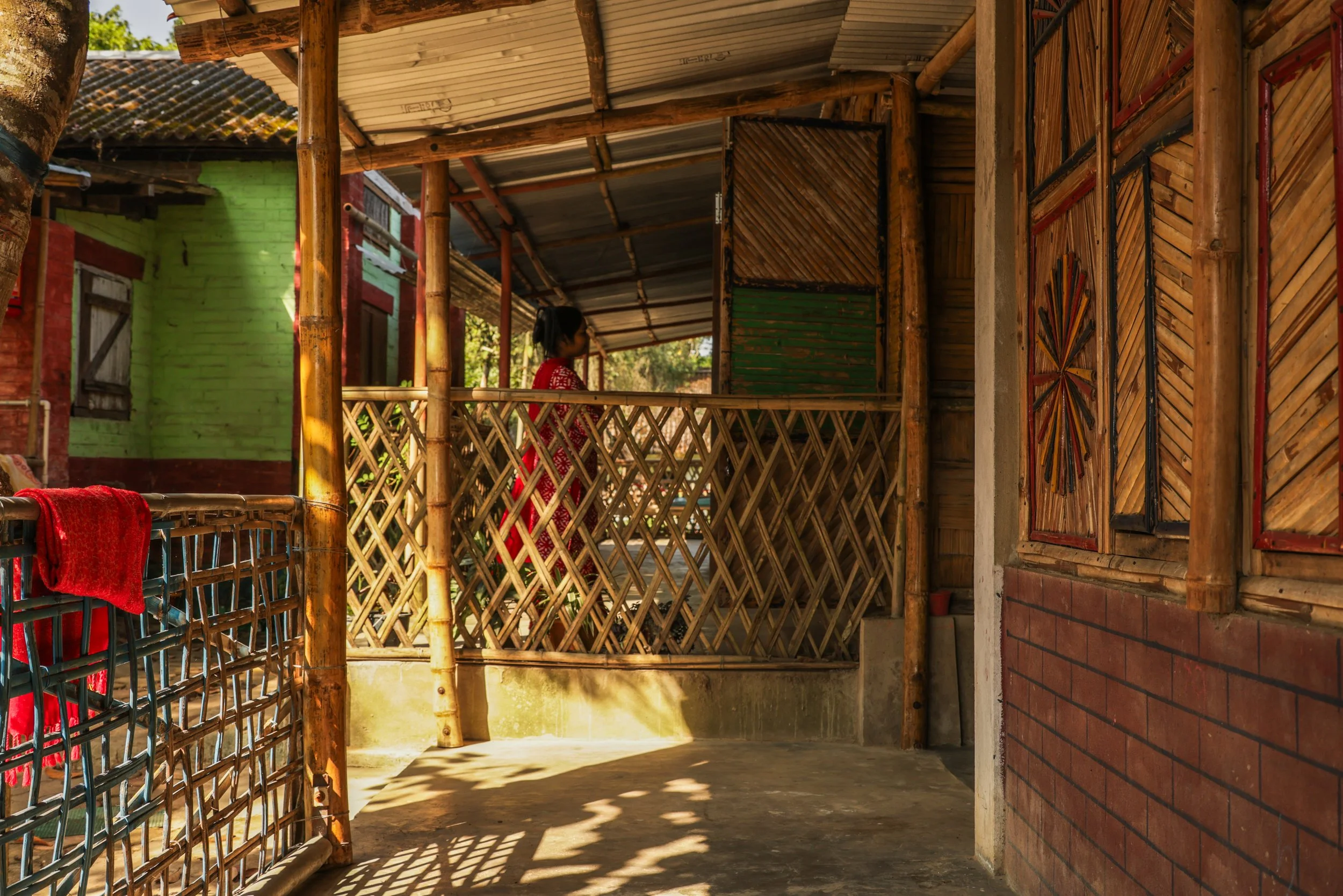 A person with dark hair smiling and a colorful macaw parrot resting on their shoulder, inside a rustic wooden structure.