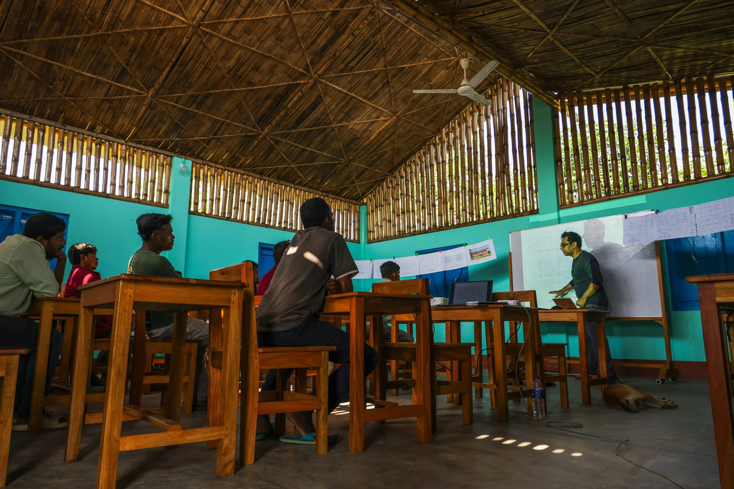 an architect presents drawings to a group of builders in a classroom setting