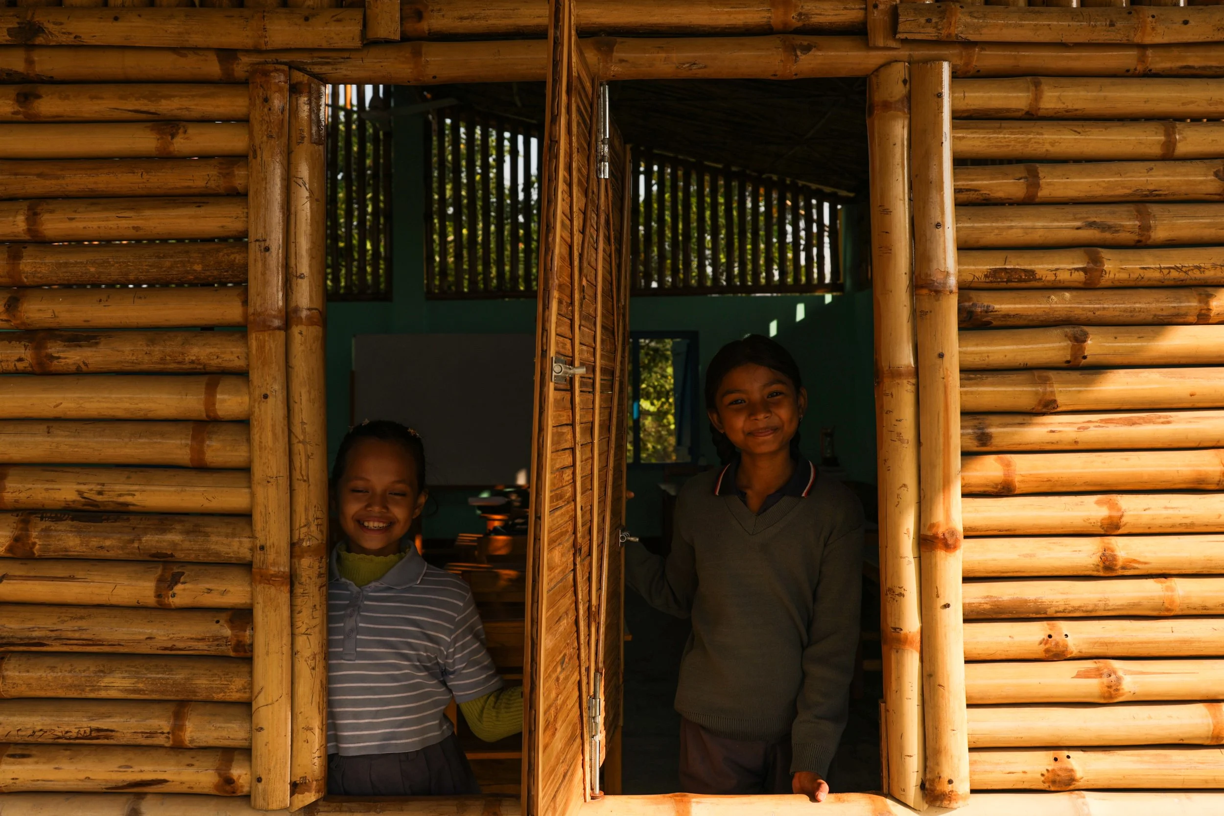 two kids inside a bamboo building looking through a window