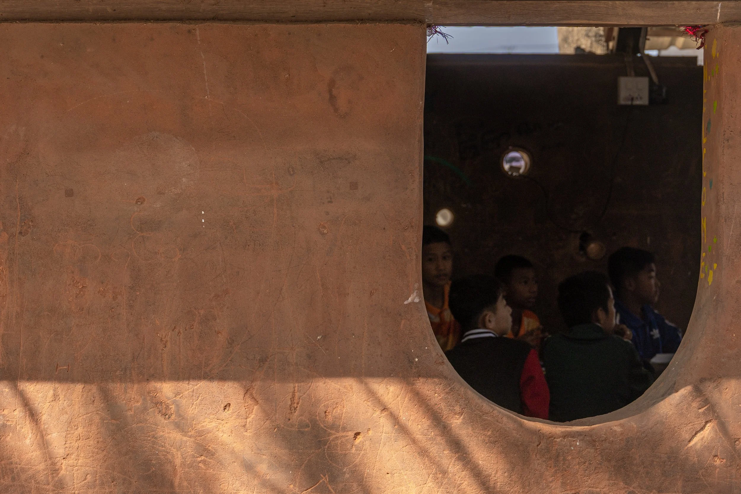 A person with dark hair smiling and a colorful macaw parrot resting on their shoulder, inside a rustic wooden structure.