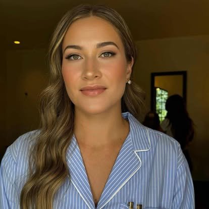 A woman with long, wavy brown hair wearing a blue and white striped pajama top, looking directly at the camera with a neutral expression.