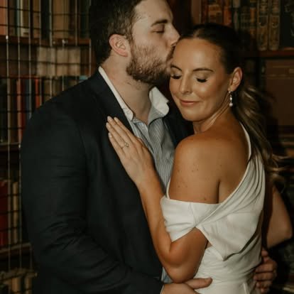 A man kisses a woman on the temple in a library setting.