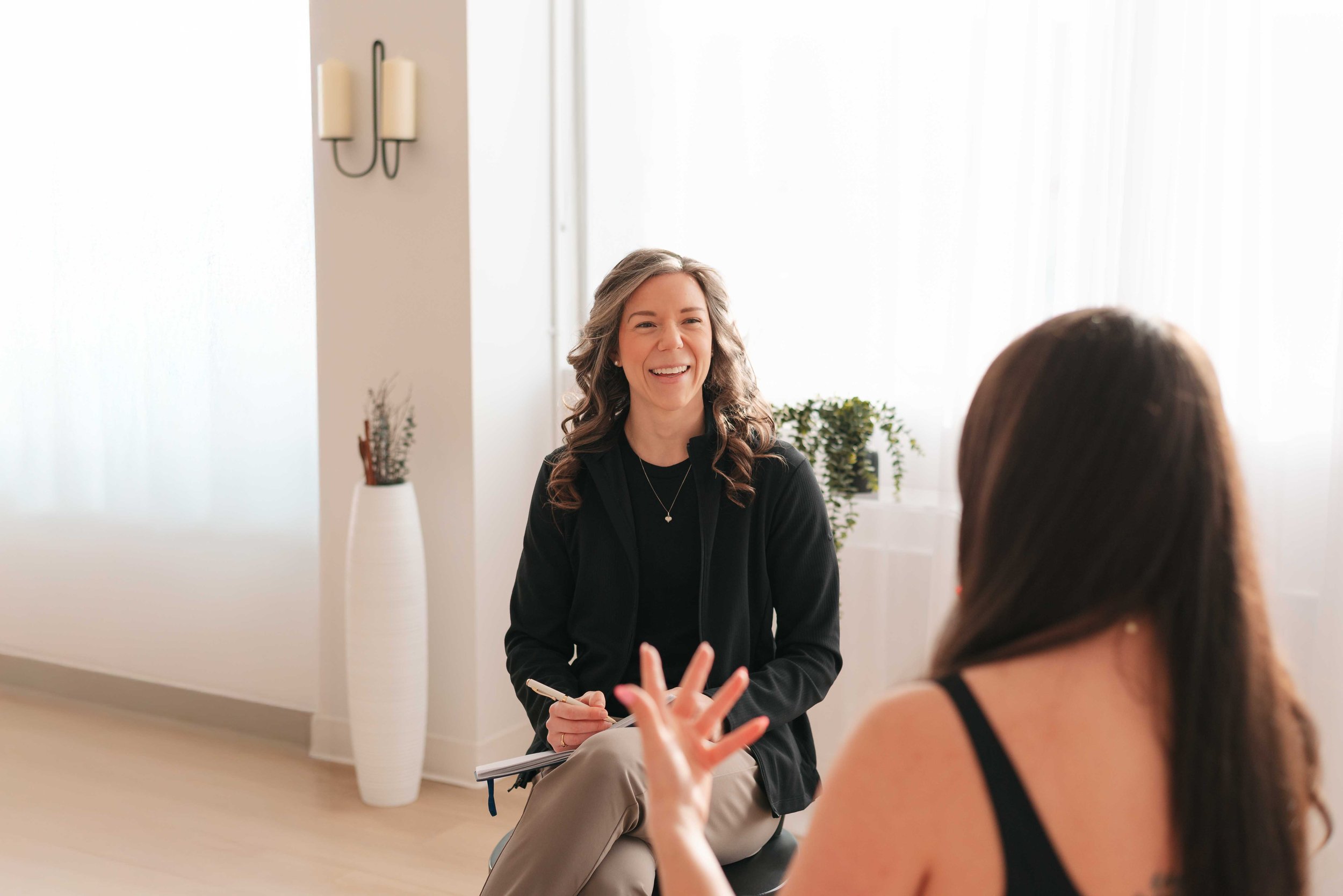 Two women having a conversation in a bright, modern room with white walls and decorative plants.