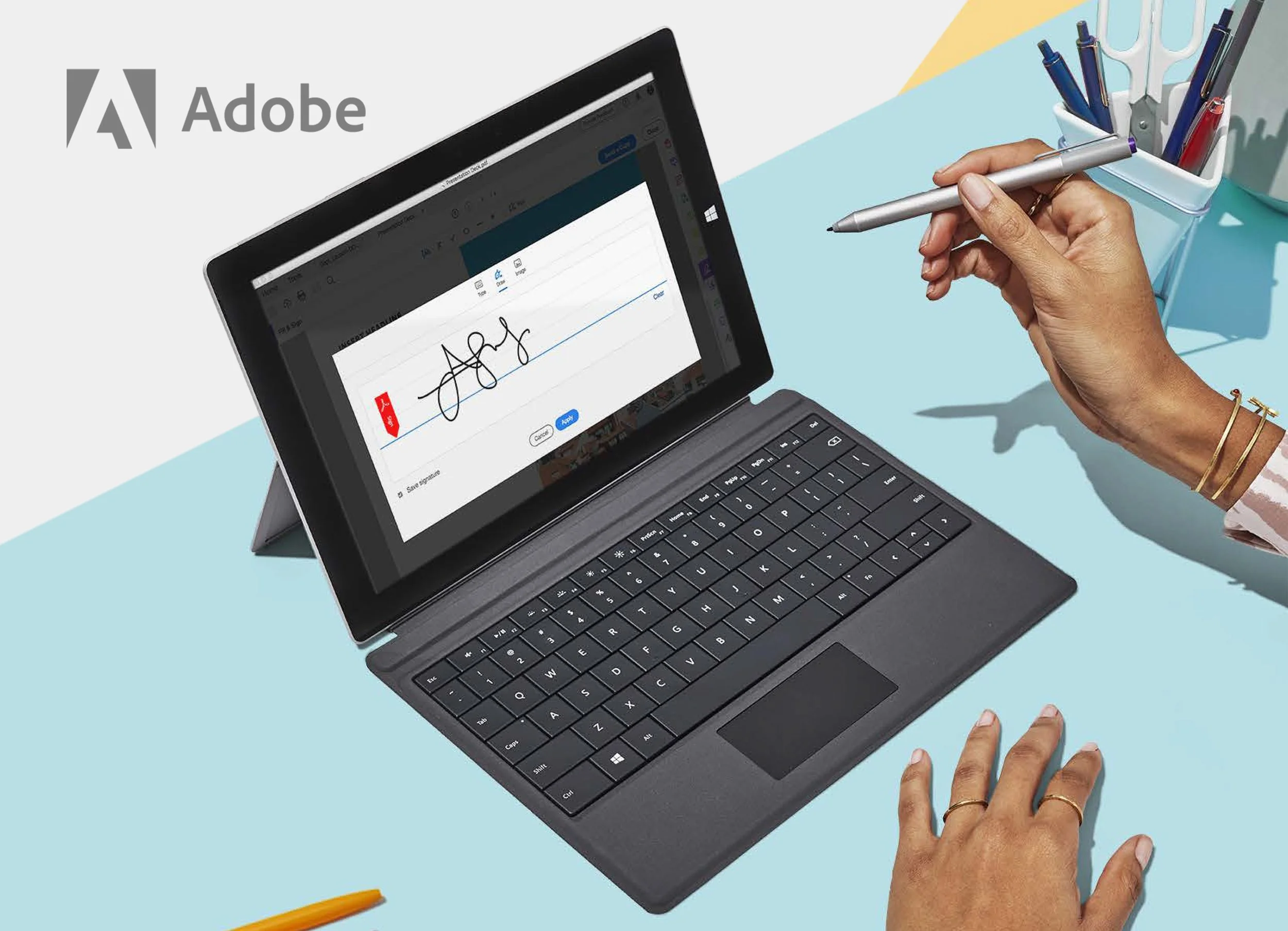 Person writing the word 'joy' on a tablet screen with a stylus, with a blue and yellow pen holder on the desk.