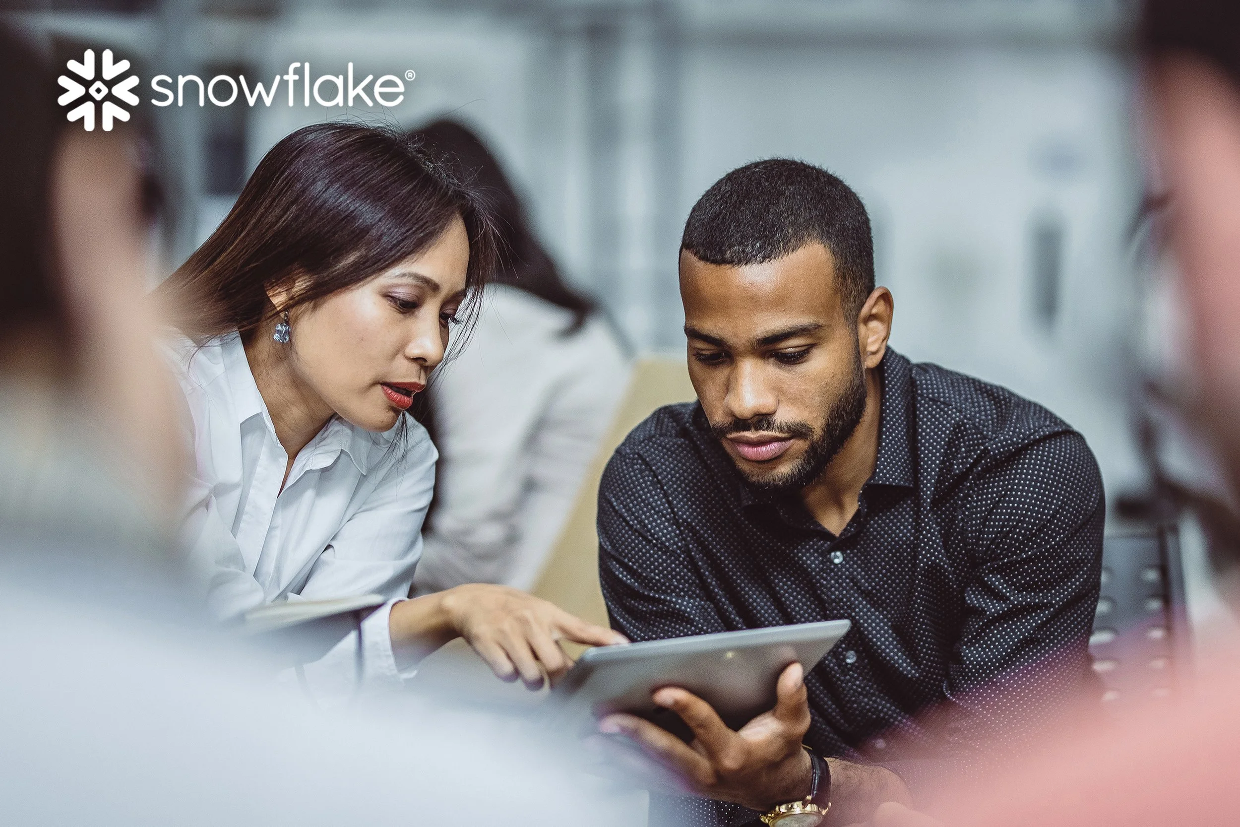 Two coworkers working together on a tablet implementing software by Snowflake.