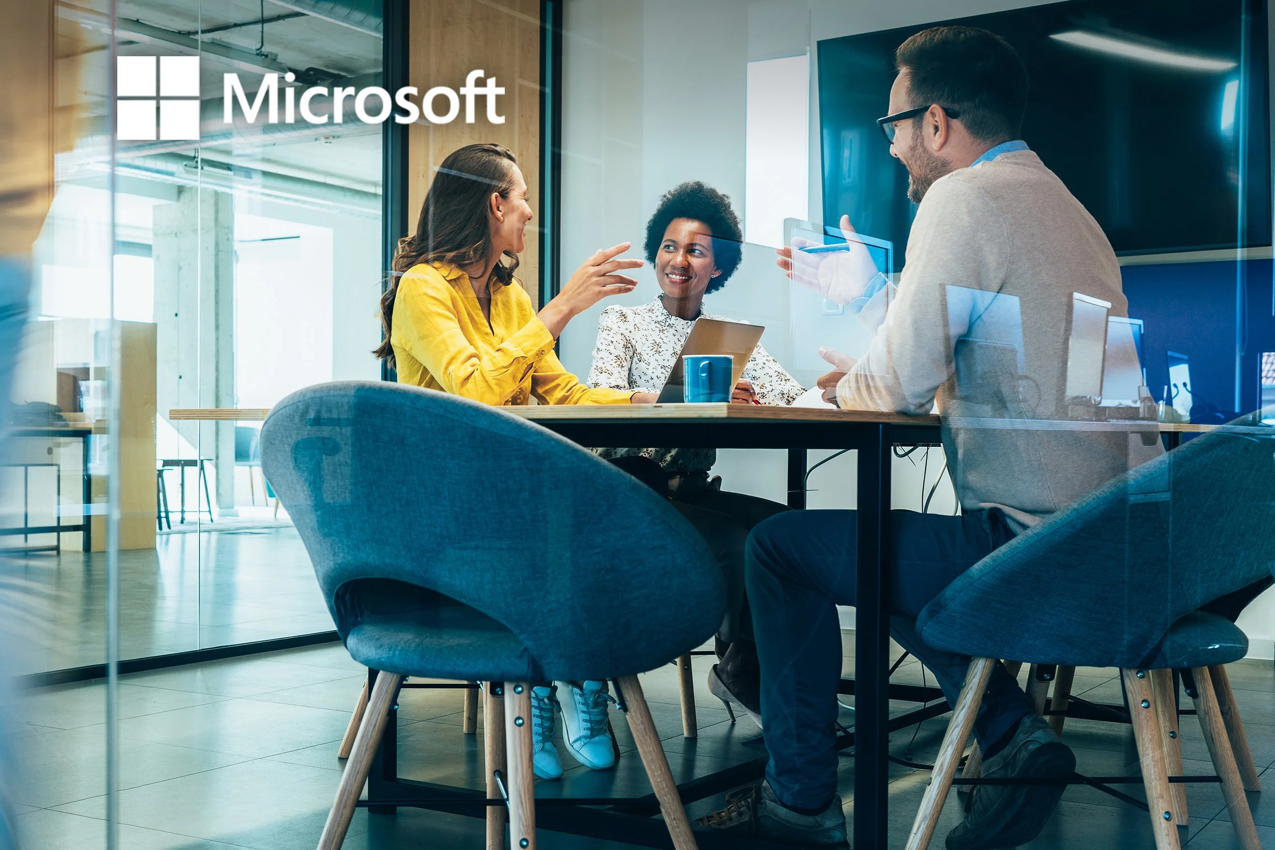 Three people in business casual attire are sitting around a table in a modern office, engaging in a discussion.
