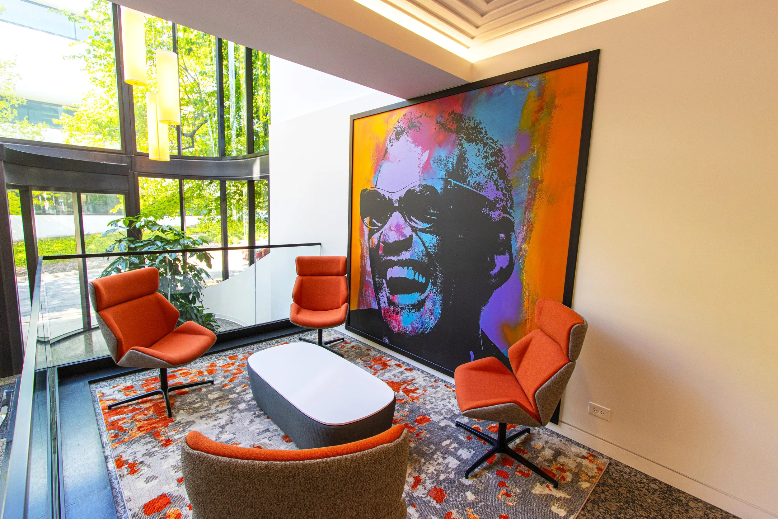 Modern office meeting area with orange chairs, abstract art on the wall, and large windows with a view of greenery.