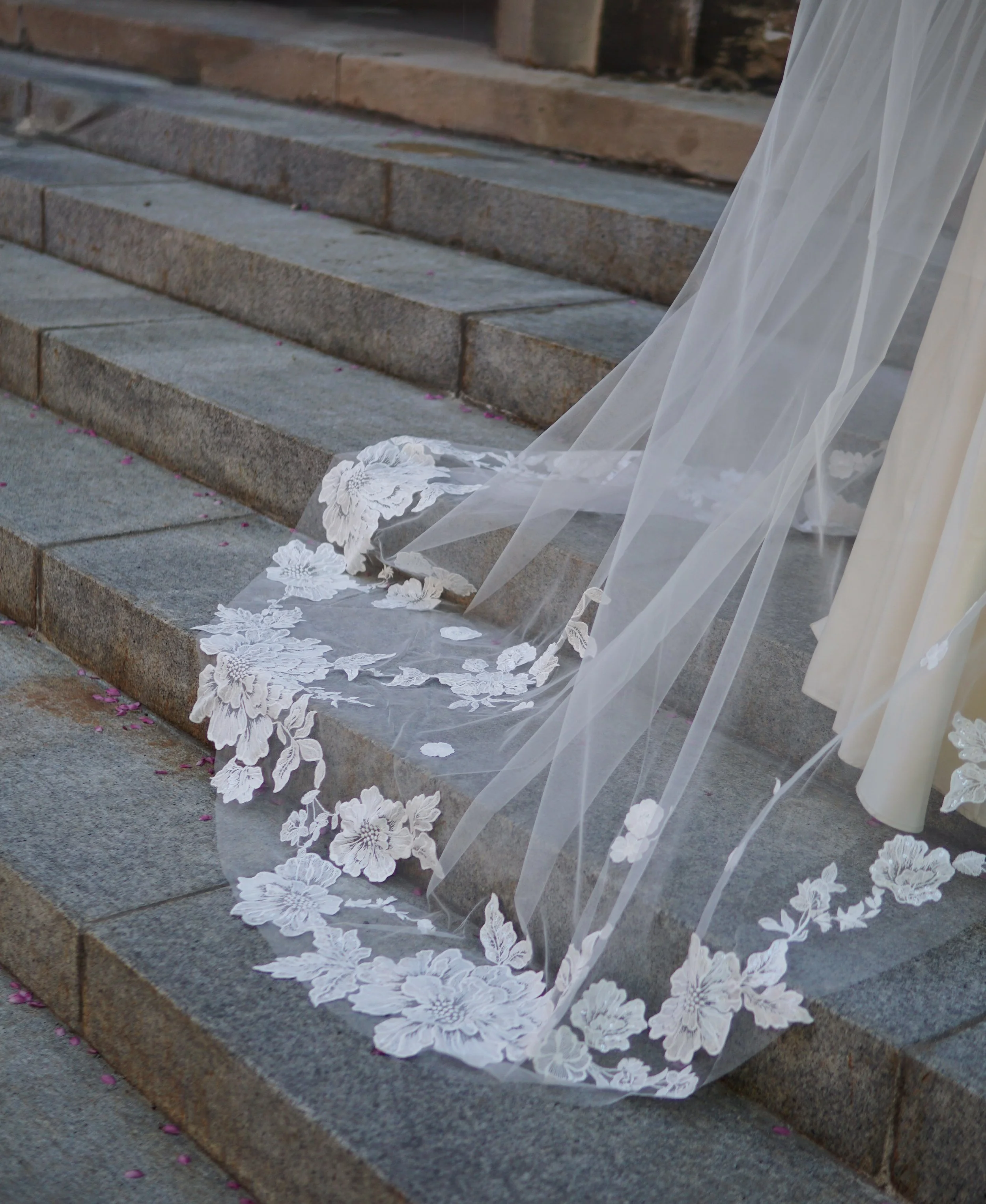The photo shows part of the veil laid on a stone stairs, highlighting the large and small floral lace appliqués in detail.