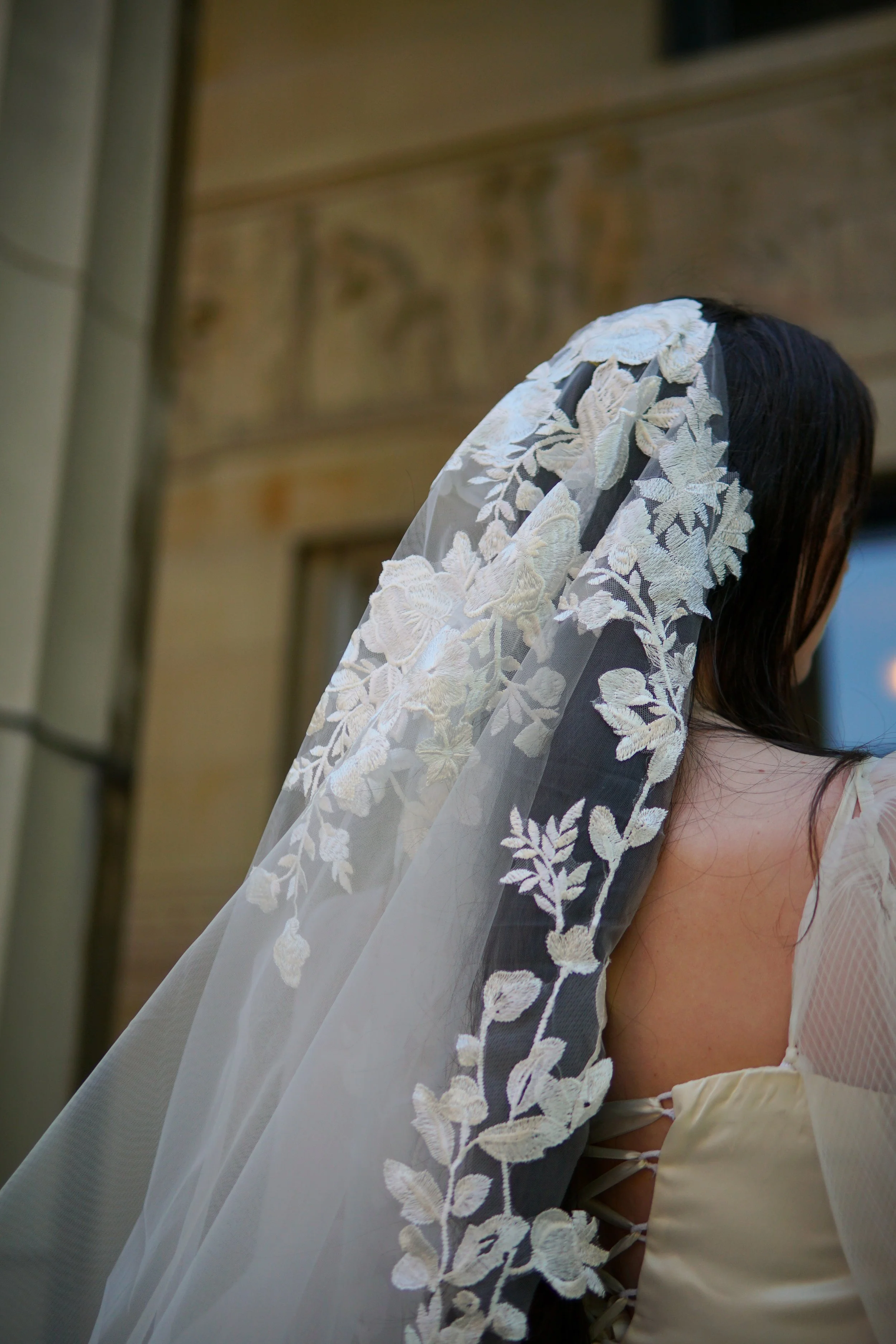 Close-up detail of the Lucia Mantilla veil showcasing intricate lace at the head area, featuring a delicate mix of small and large floral motifs and branching botanical patterns.