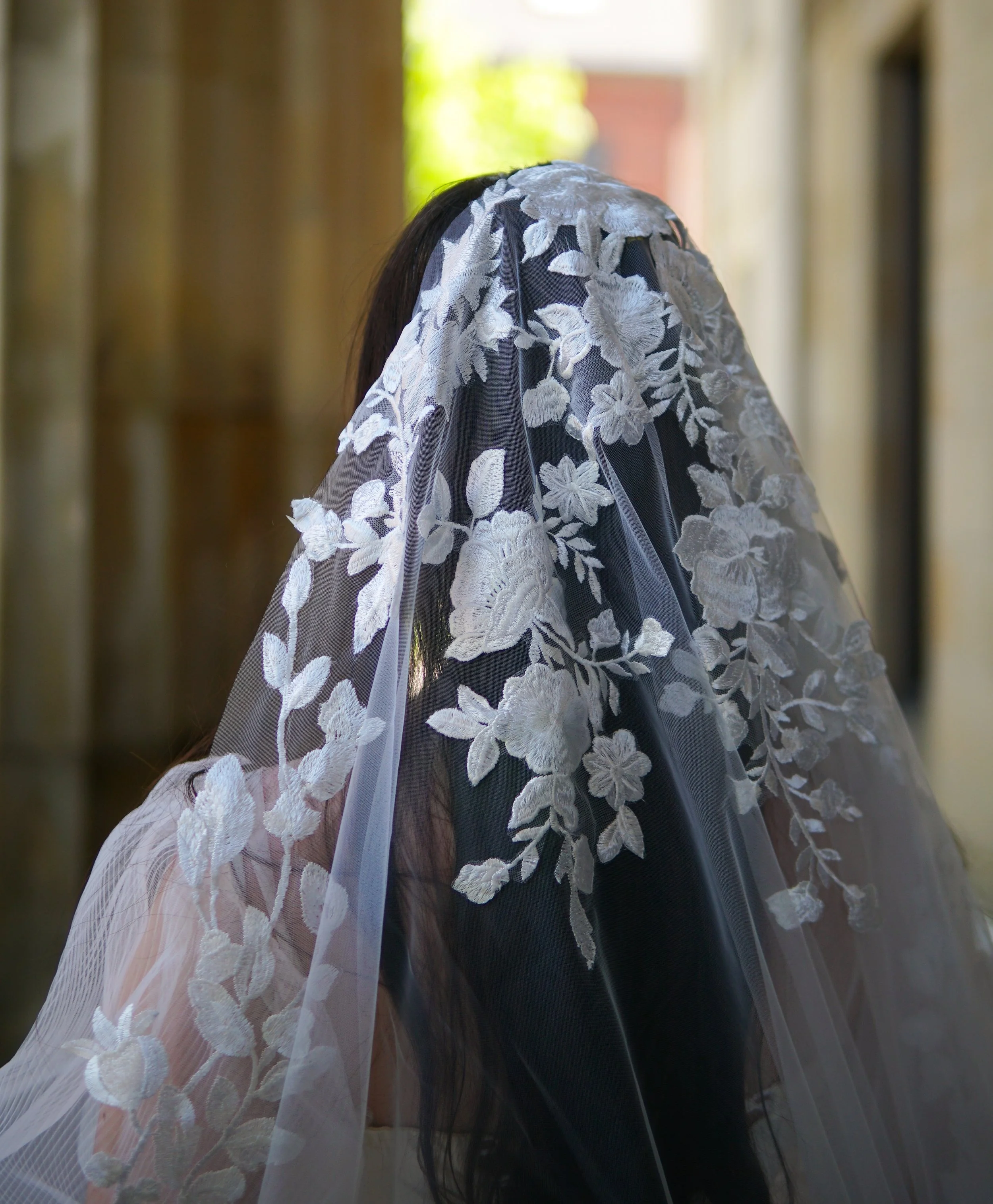 Close-up detail of the Lucia Mantilla veil showcasing intricate lace at the head area, featuring a delicate mix of small and large floral motifs and branching botanical patterns.