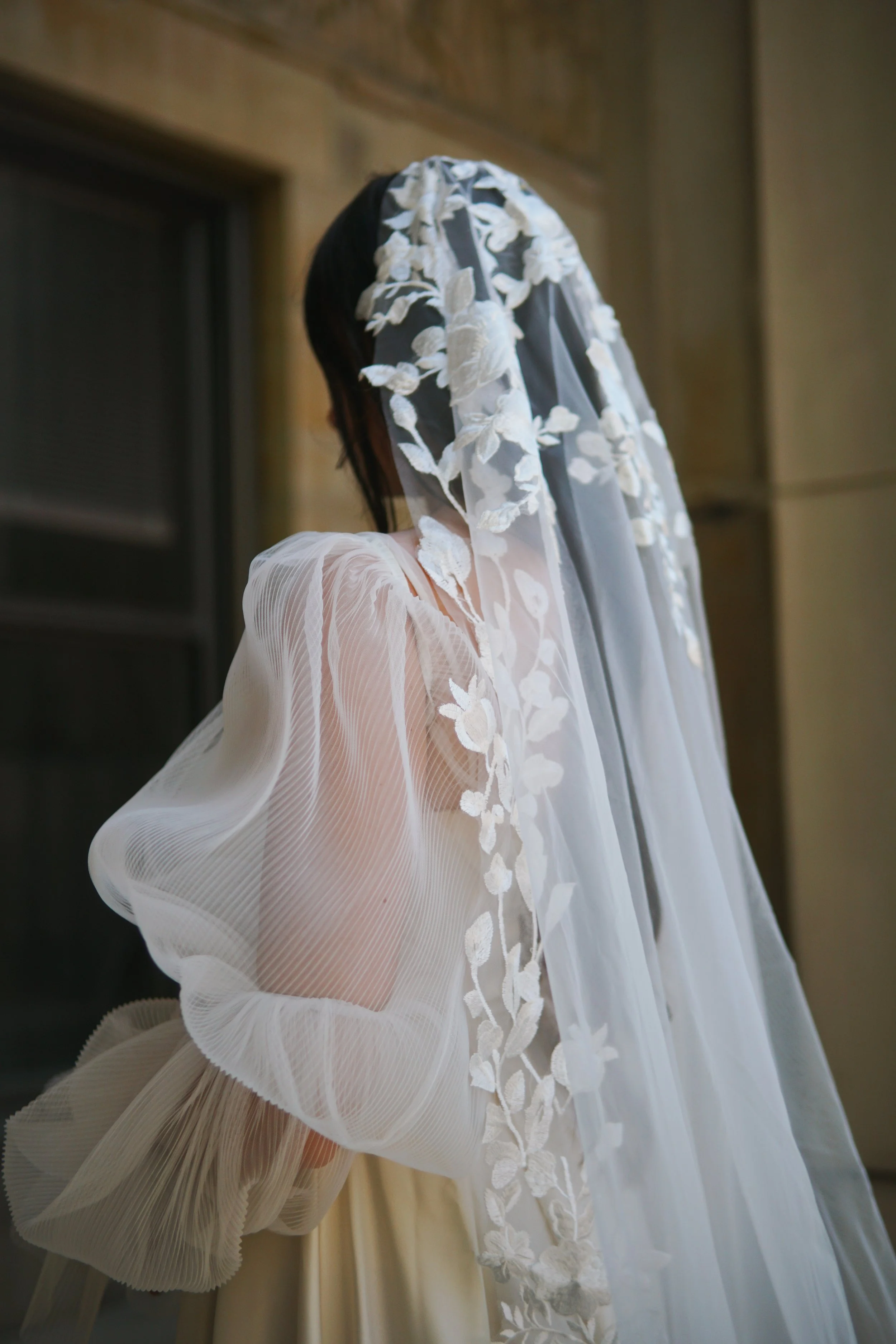 Close-up detail of the Lucia Mantilla veil showcasing intricate lace at the head area, featuring a delicate mix of small and large floral motifs and branching botanical patterns.