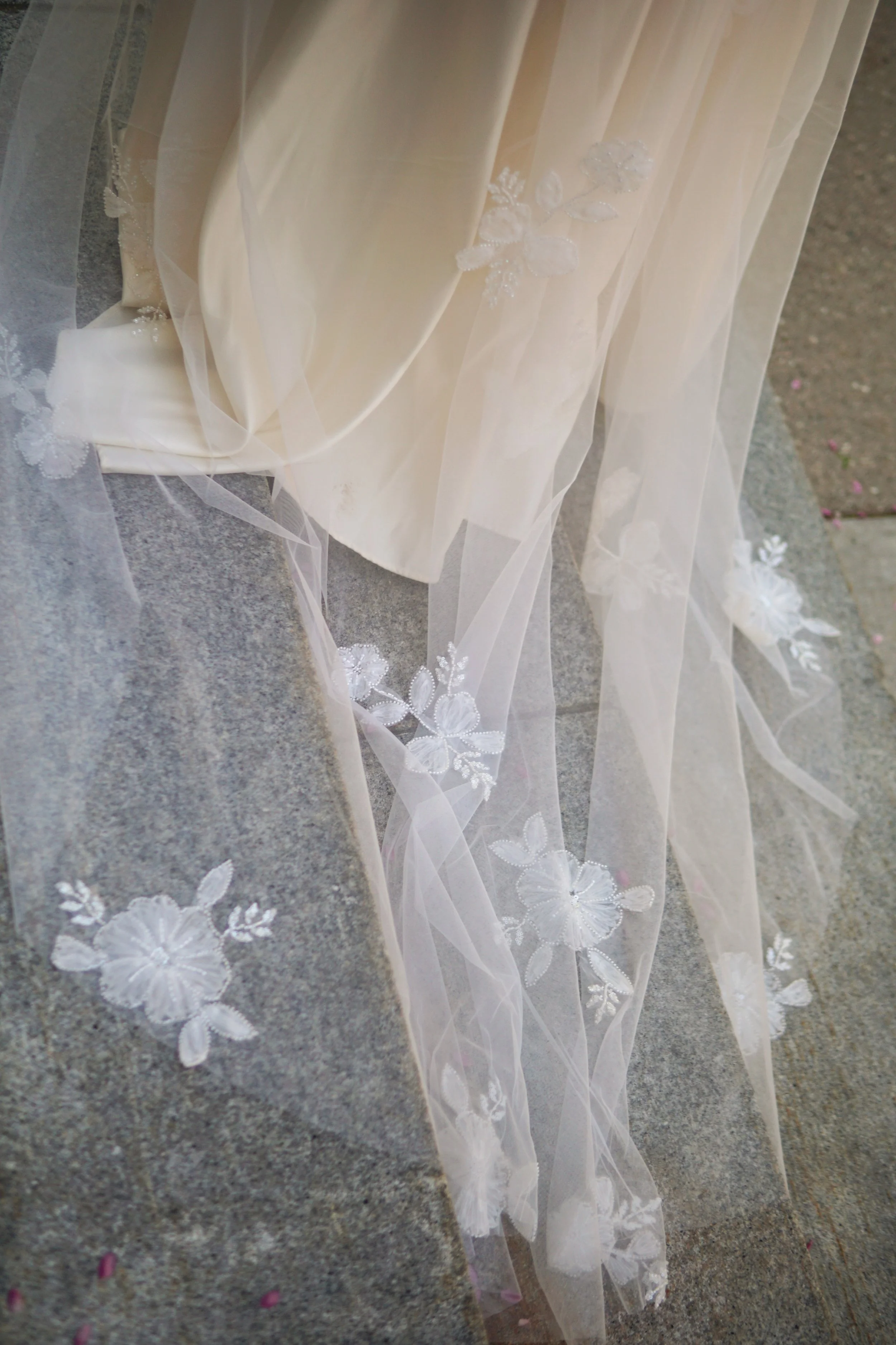 close picture of a floral beaded lace applique on the veil laying on the stone floor.