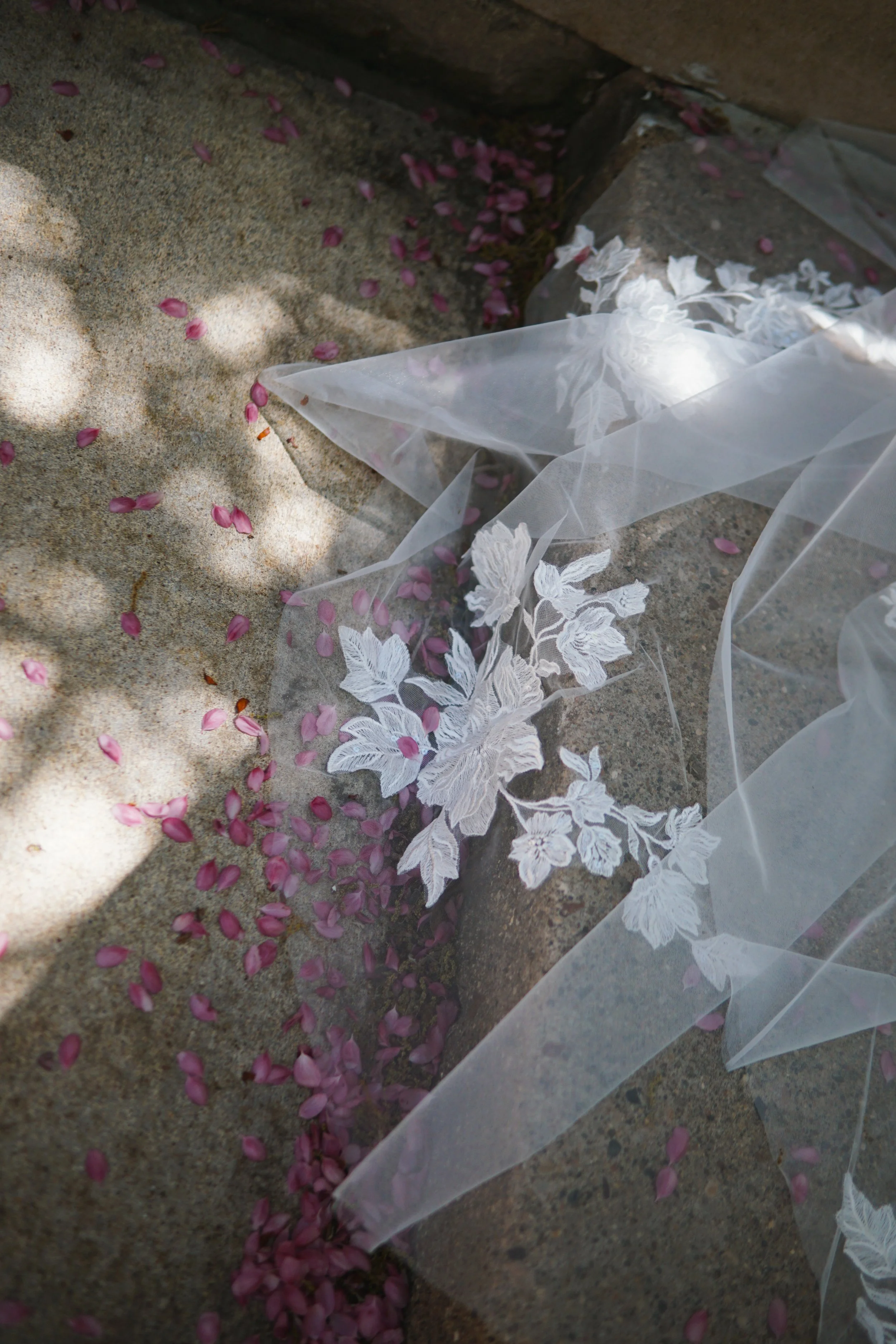 The photo shows part of the veil laid on a stone floor, highlighting one large floral lace appliqué in detail.