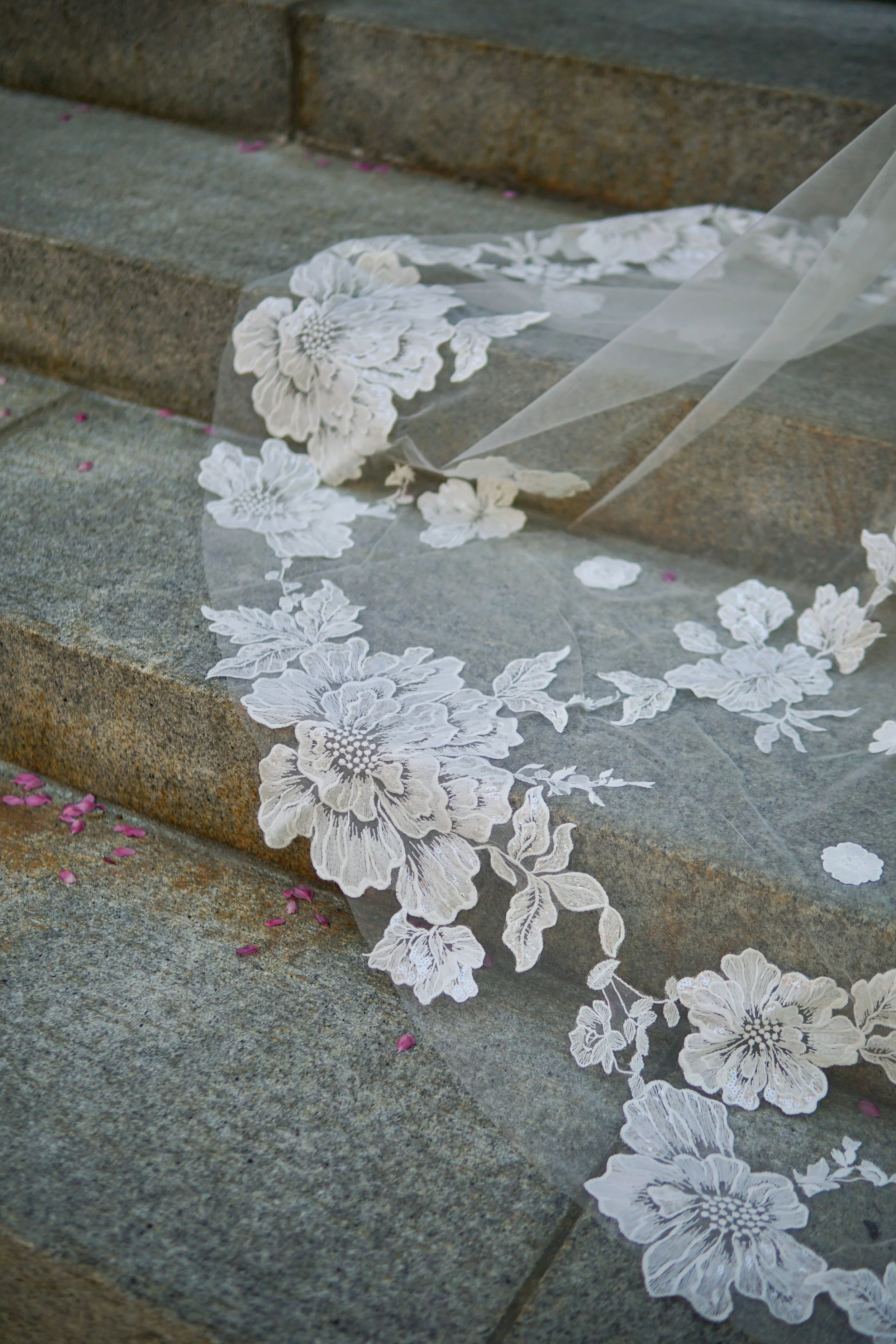 The photo shows part of the veil laid on a stone stairs, highlighting the large and small floral lace appliqués in detail.