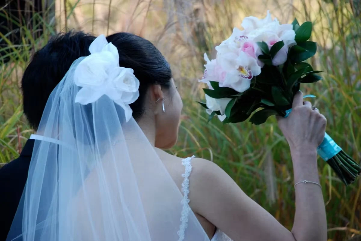 Bride holding a bouquet of white and pink flowers in an outdoor setting.