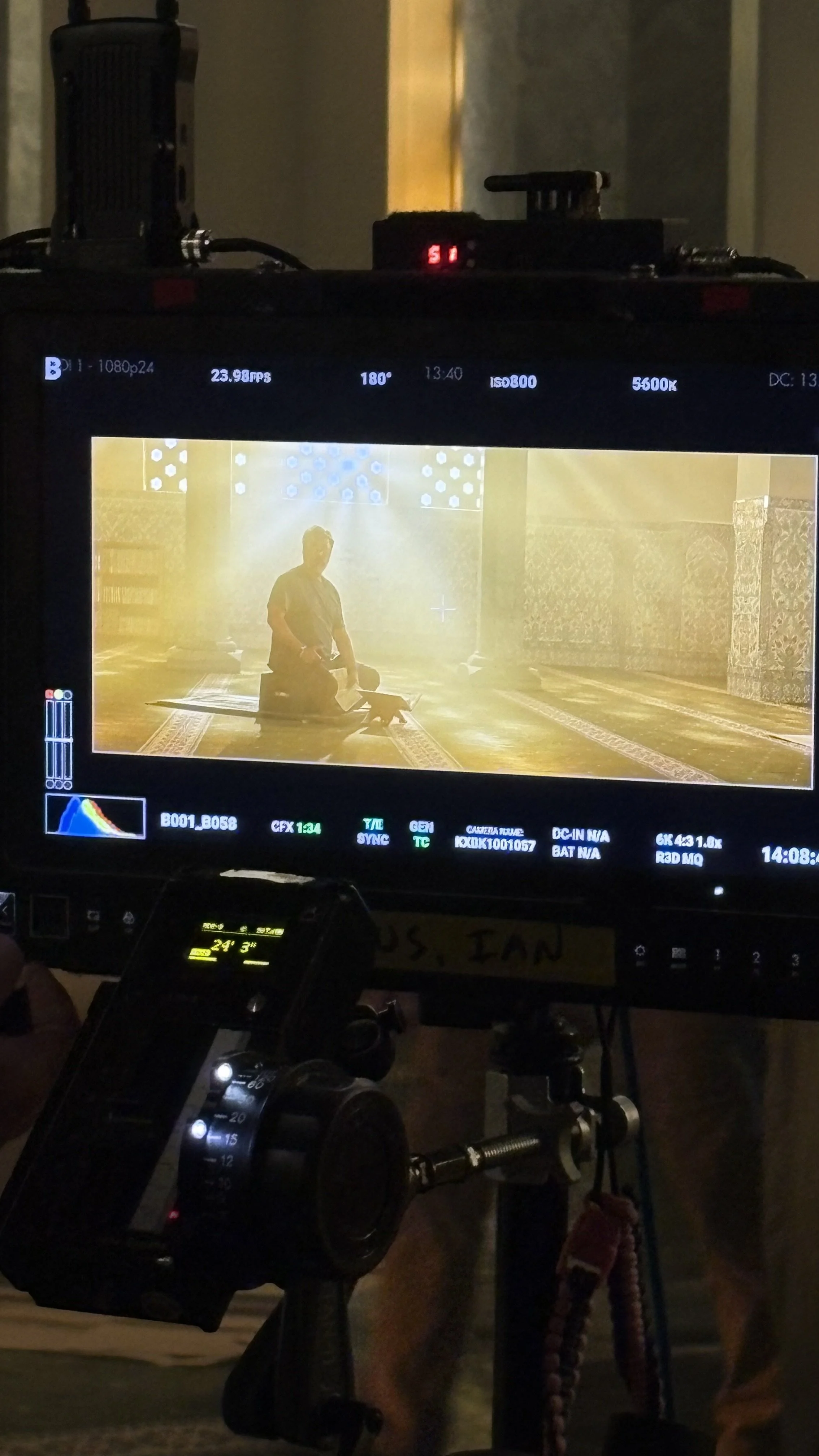 Grip Work: Feature Film
Photo of a video camera monitor showing a man kneeling in prayer inside a mosque, illuminated by sunlight rigged condor lights streaming through windows.