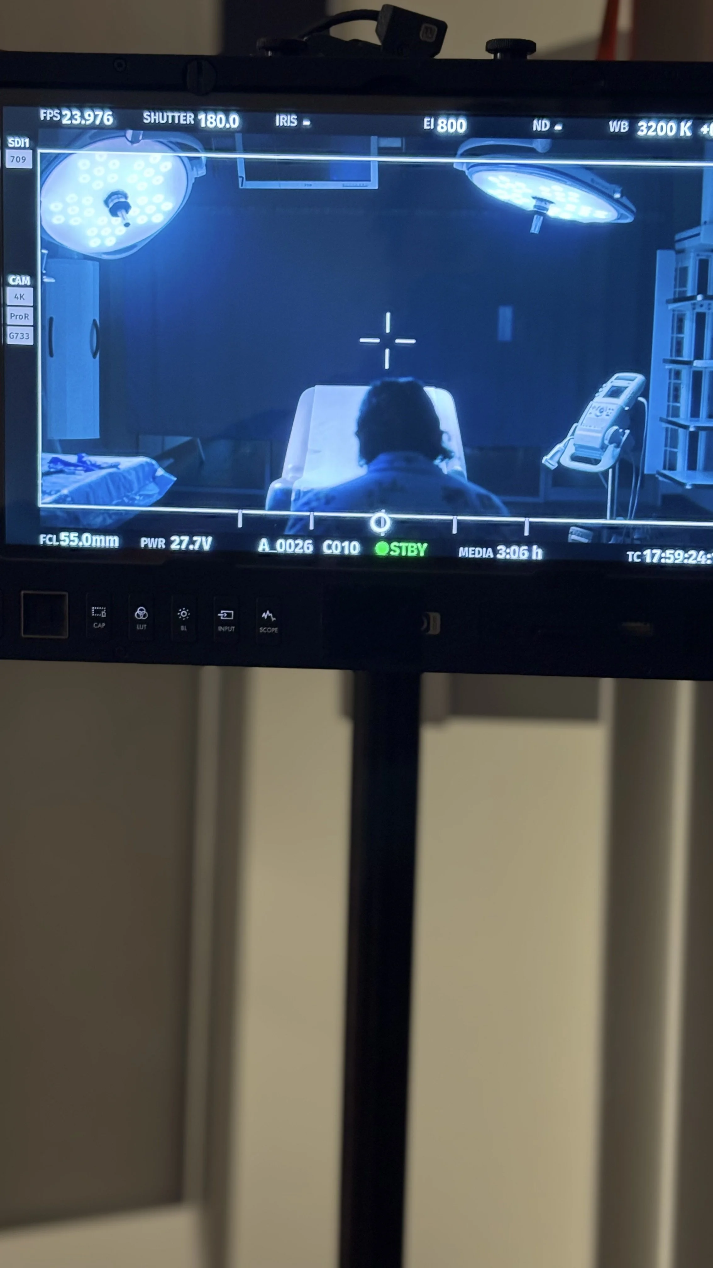 View through a monitor showing a medical examination room with a patient lying on an examination table, a medical lamp overhead, and a telephone on a small table. 
Specialty Cuts of Diffusion